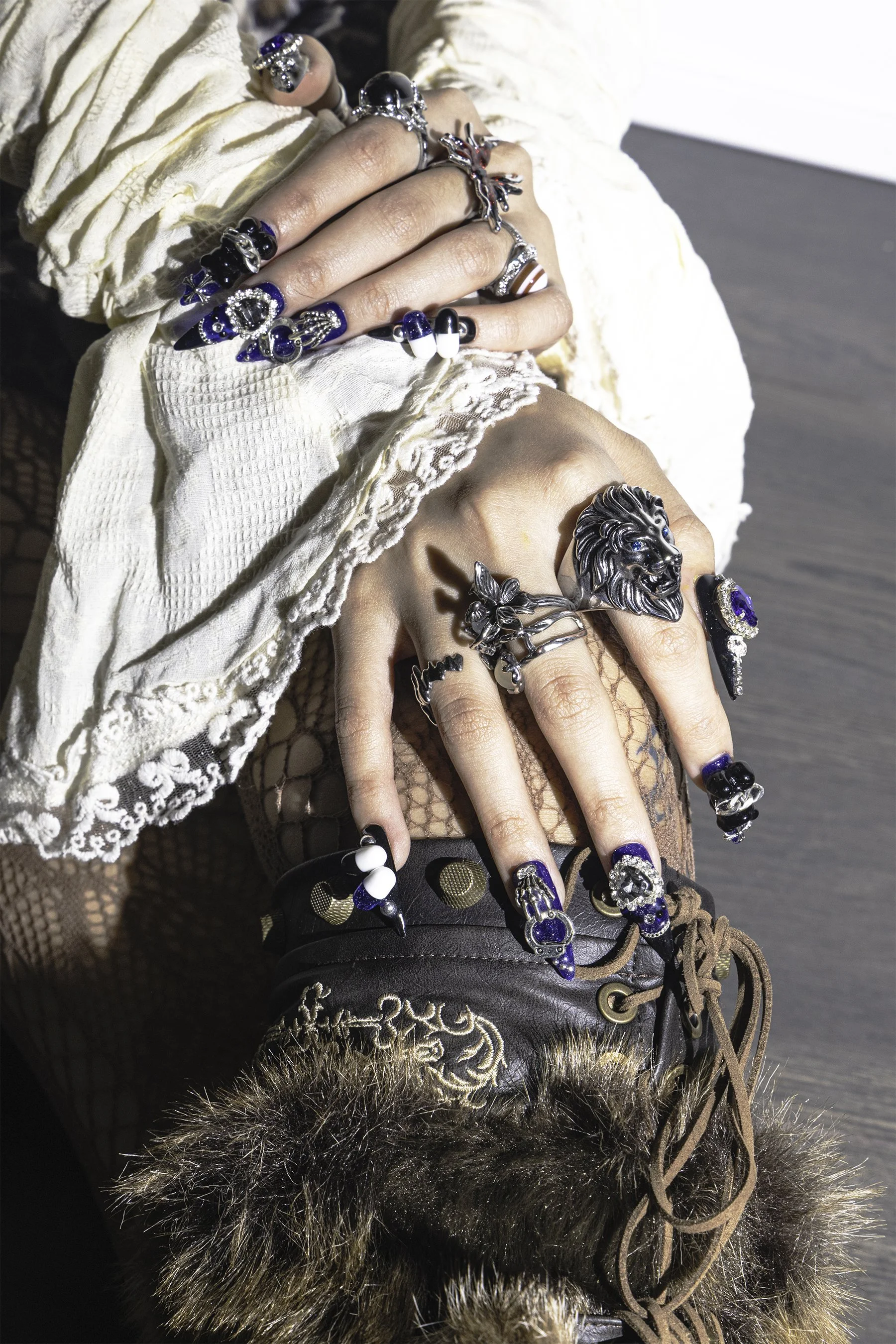 Hands with blue nail designs and rings resting on legs