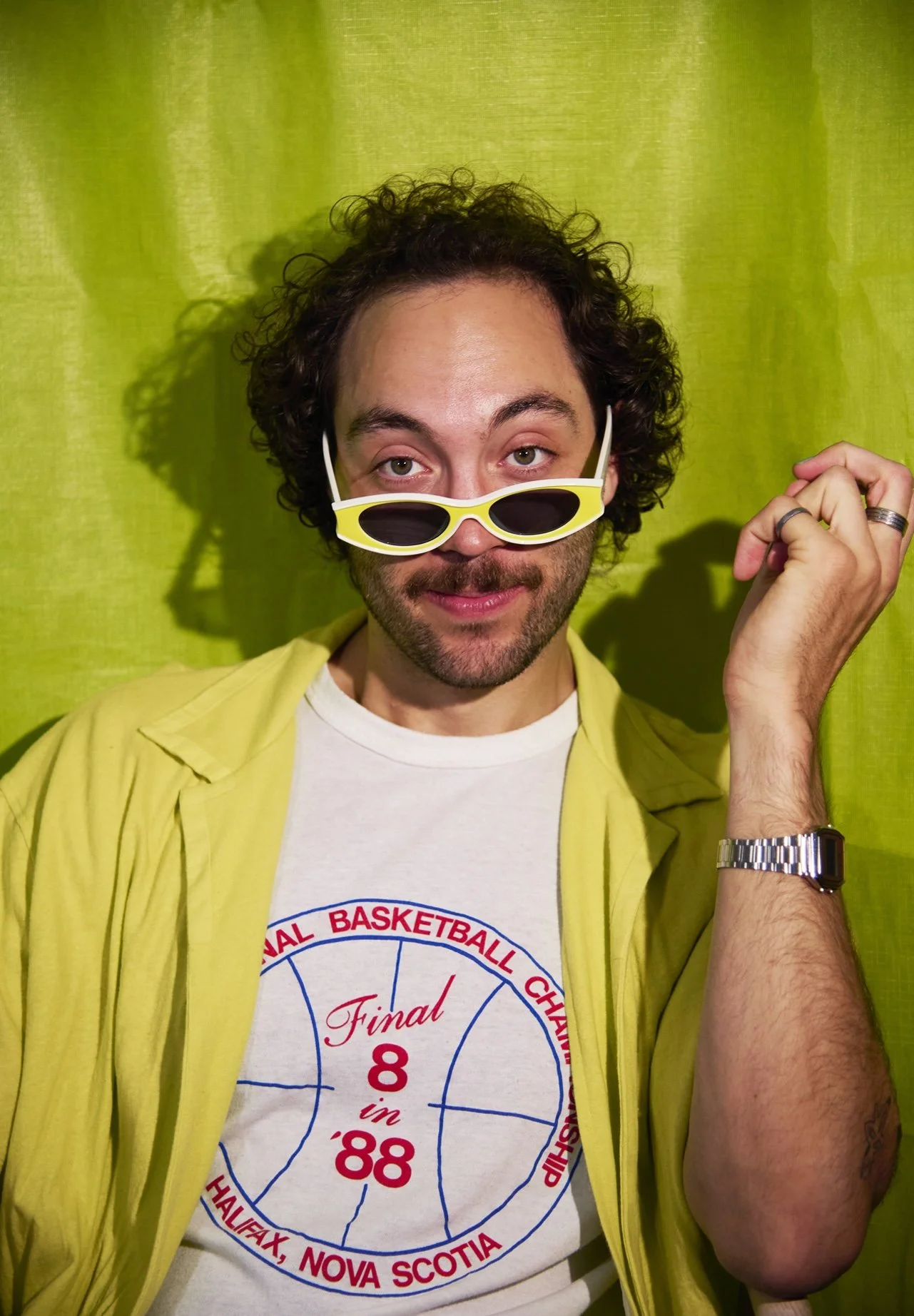 White man wearing baseball hat and sunglasses looking directly into camera. Lime green background