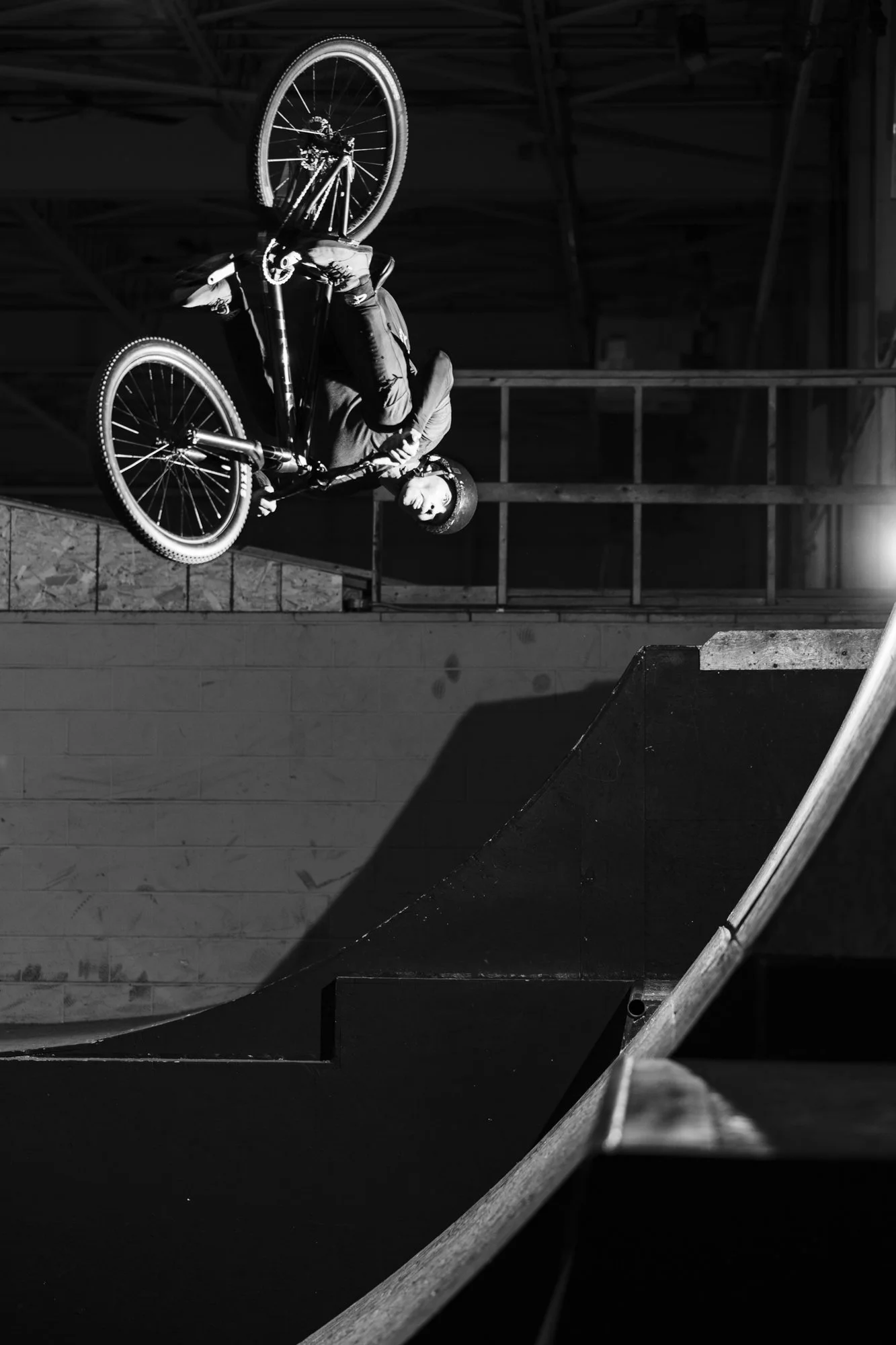 Man on mountain bike doing trick upside down in air, indoor skatepark, black and white