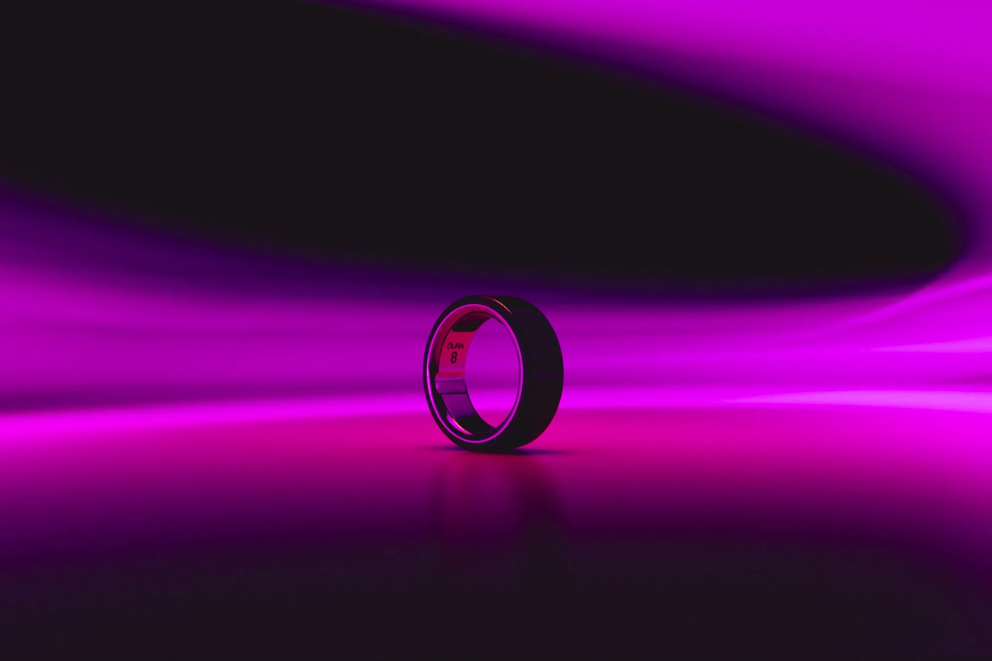 Neon magenta ring on reflective surface with soft gradient lighting.