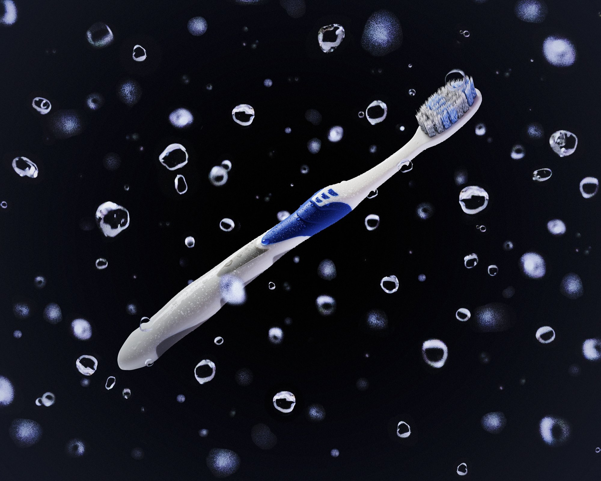Wet White Toothbrush floating in darkness, surrounded by suspended water droplets.