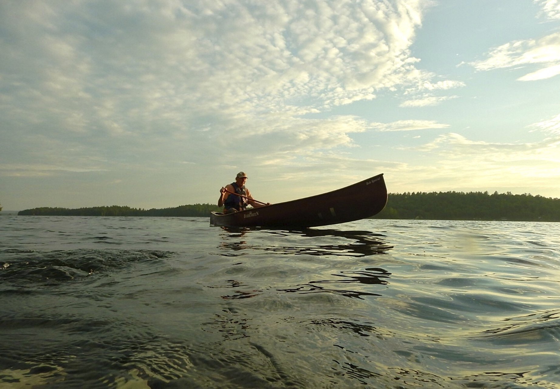 Old man in a canoe on water. Blue sky with clouds.
