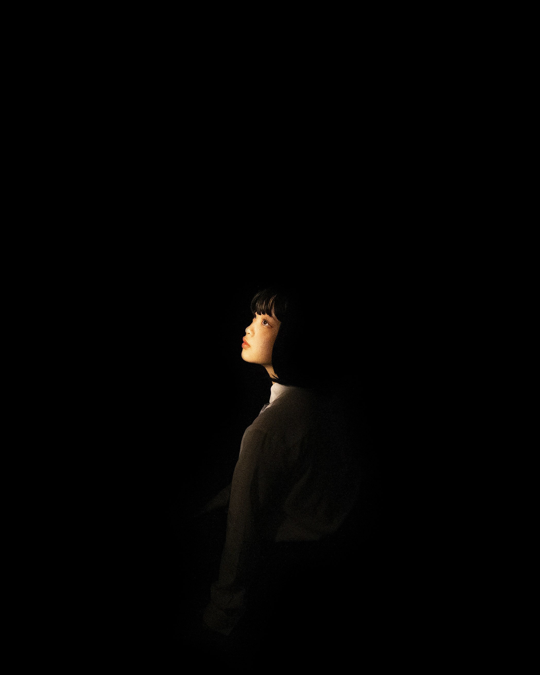 Person in profile looking upward, face illuminated against dark background.