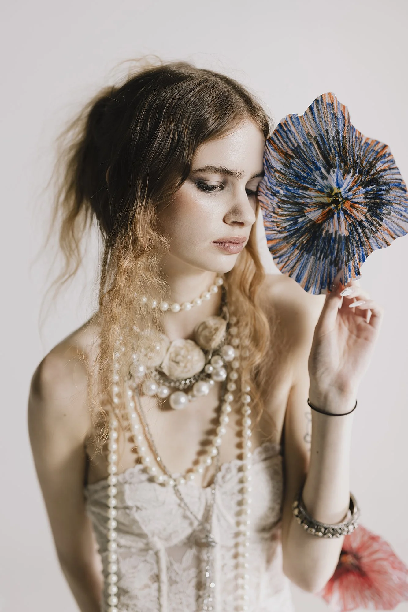 Woman holding flower, wearing pearl necklace and white lace dress, half body