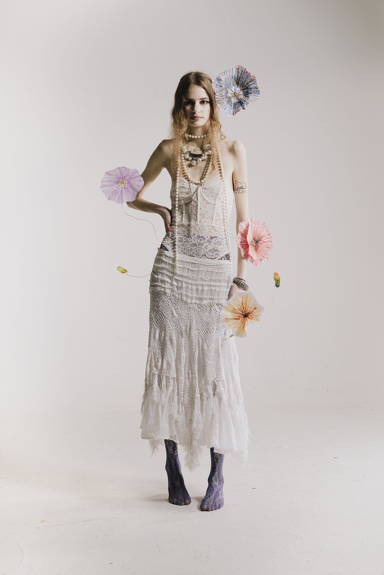 Model in white lace dress surrounded by colourful flowers, full body
