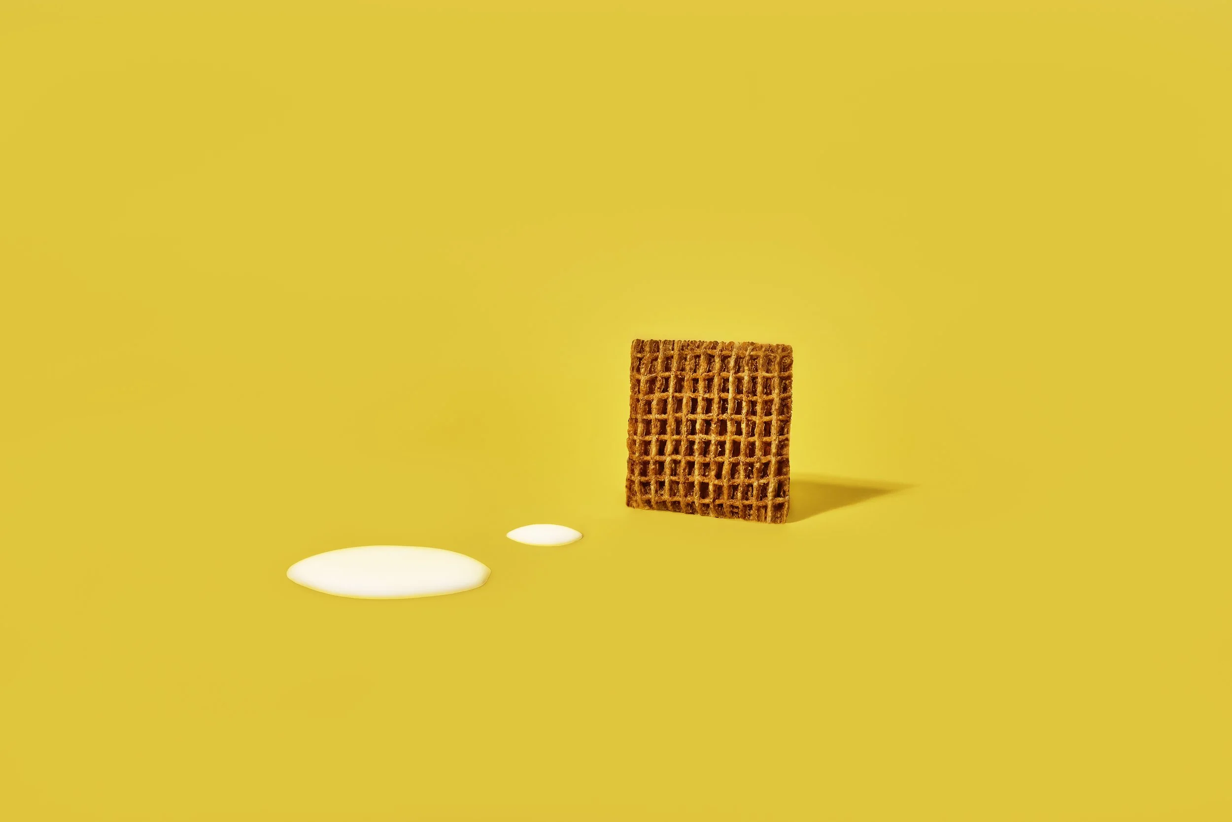 One piece of shreddies standing up in front of two white dots on yellow background.
