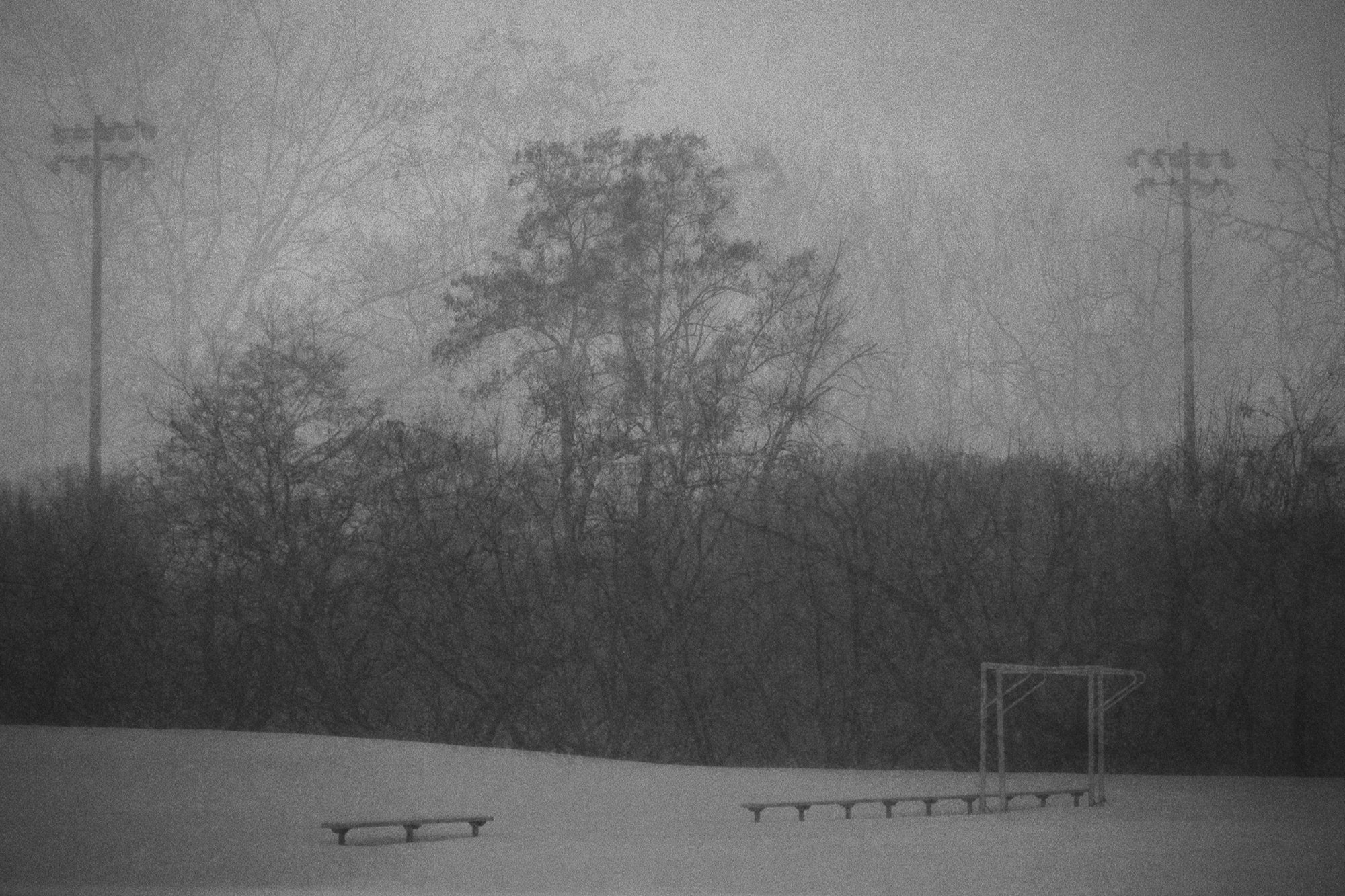 Snowy field multiple exposure, overlapping branches, field lights, soccer post, benches.