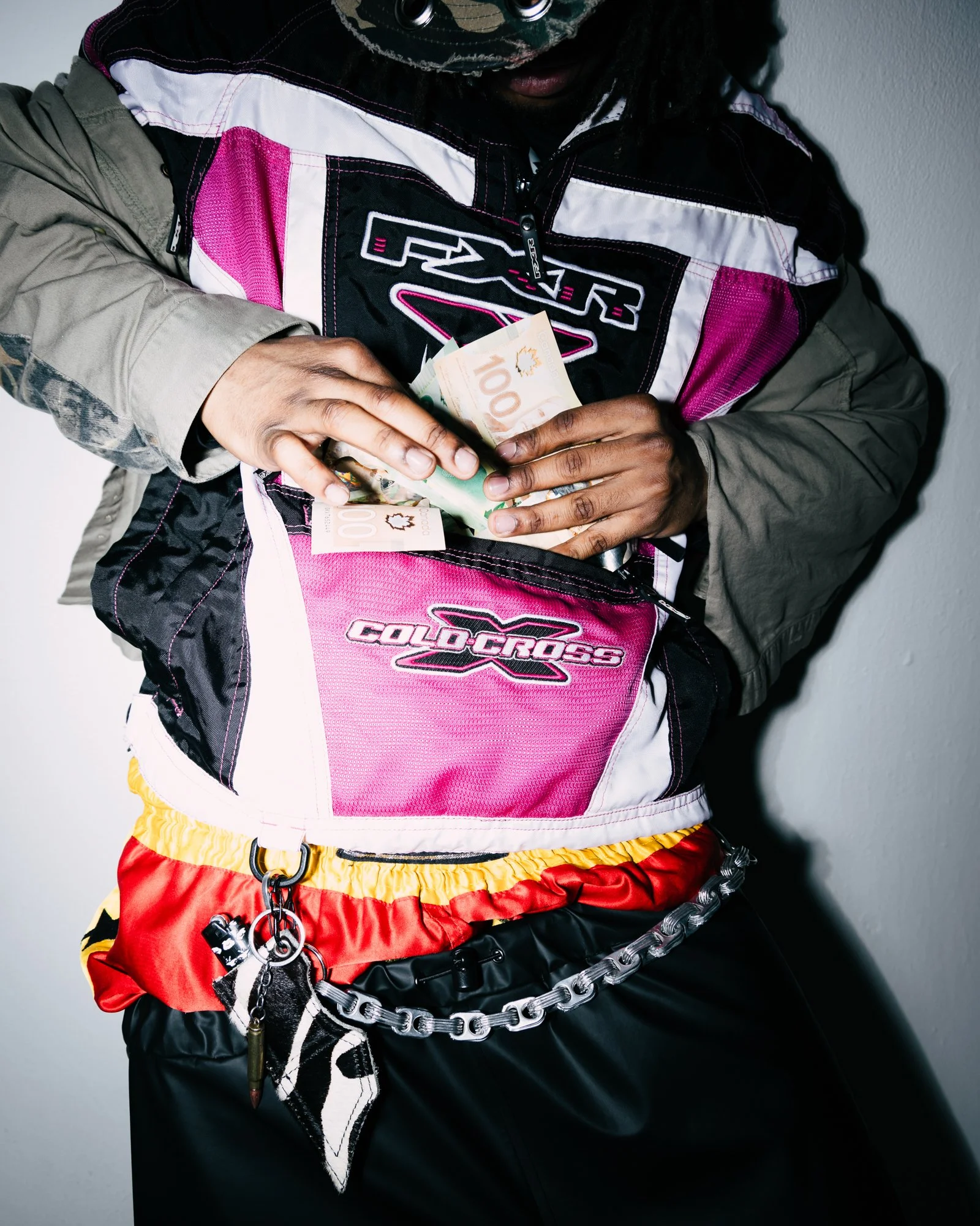 Man's torso, wearing pink snowmobile jacket, red and yellow boxers, hip chain, counting money.