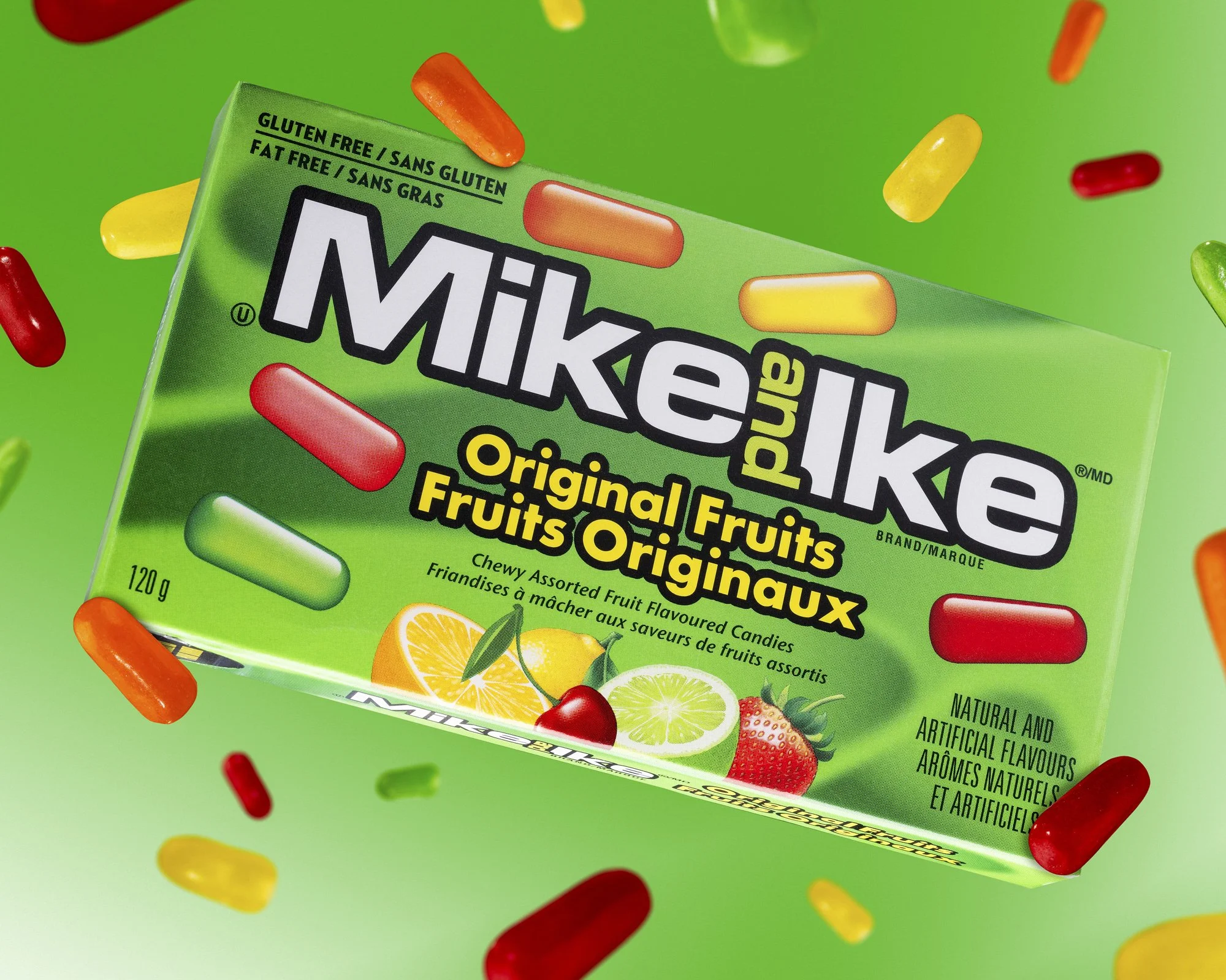 Green box of Mike and Ike original fruit flavoured candy, floating, green vibrant background, surrounded by floating pieces of Mike and Ike candy.