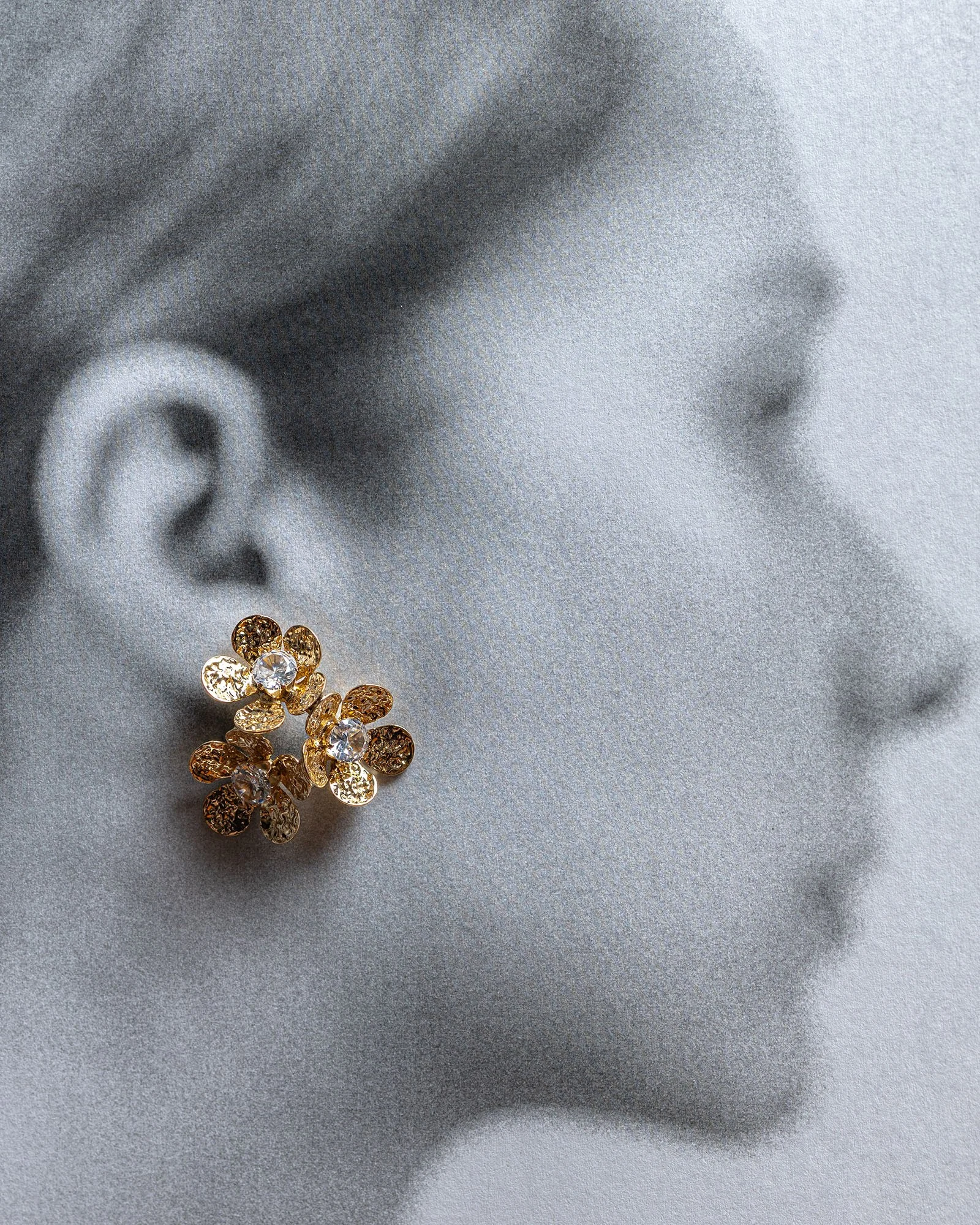 Blurred, close-up, black-and-white profile of a woman with gold floral earrings with gems on the ear.