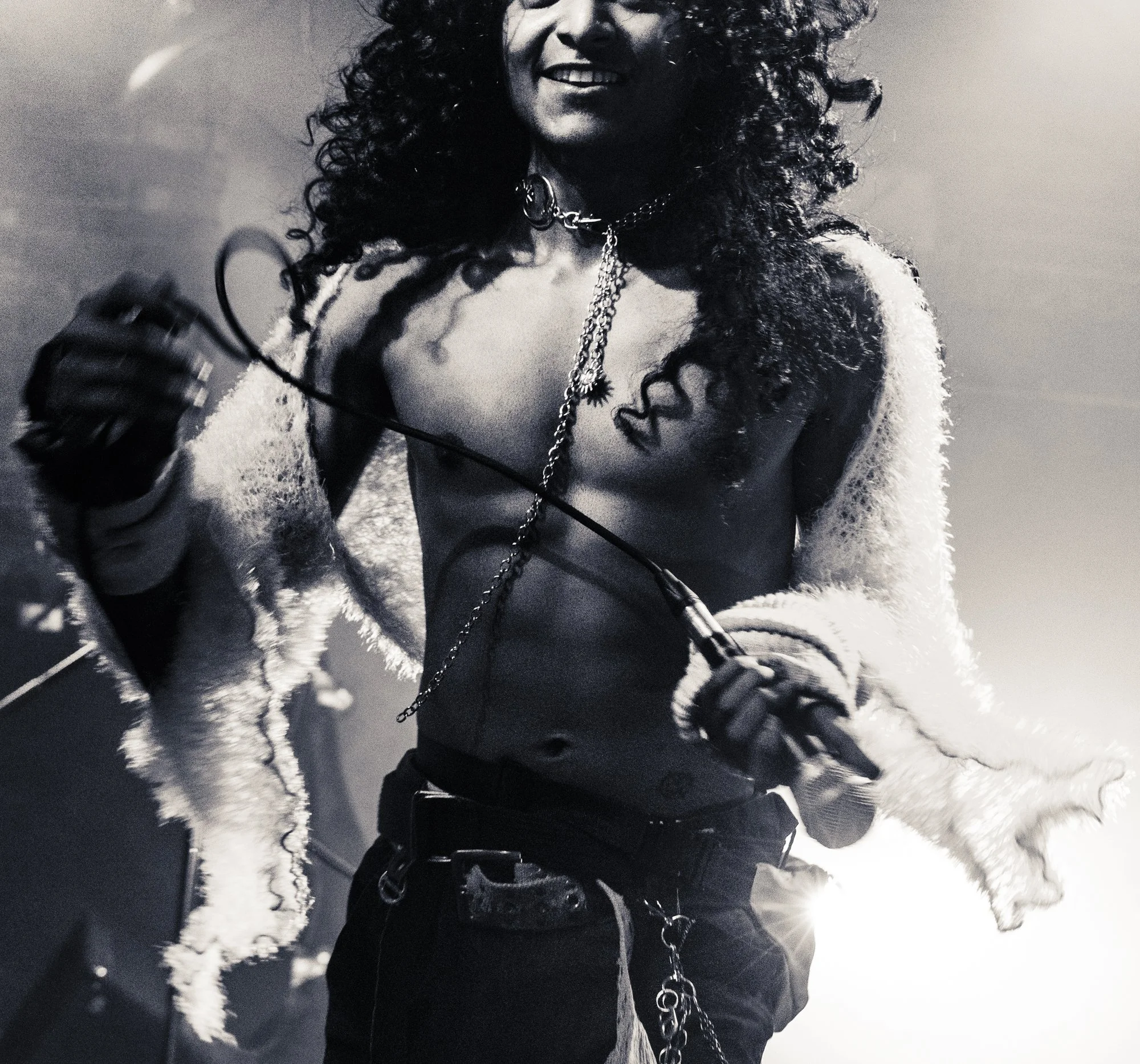 Shirtless man performing, holding microphone, eyes cut off, grainy black and white