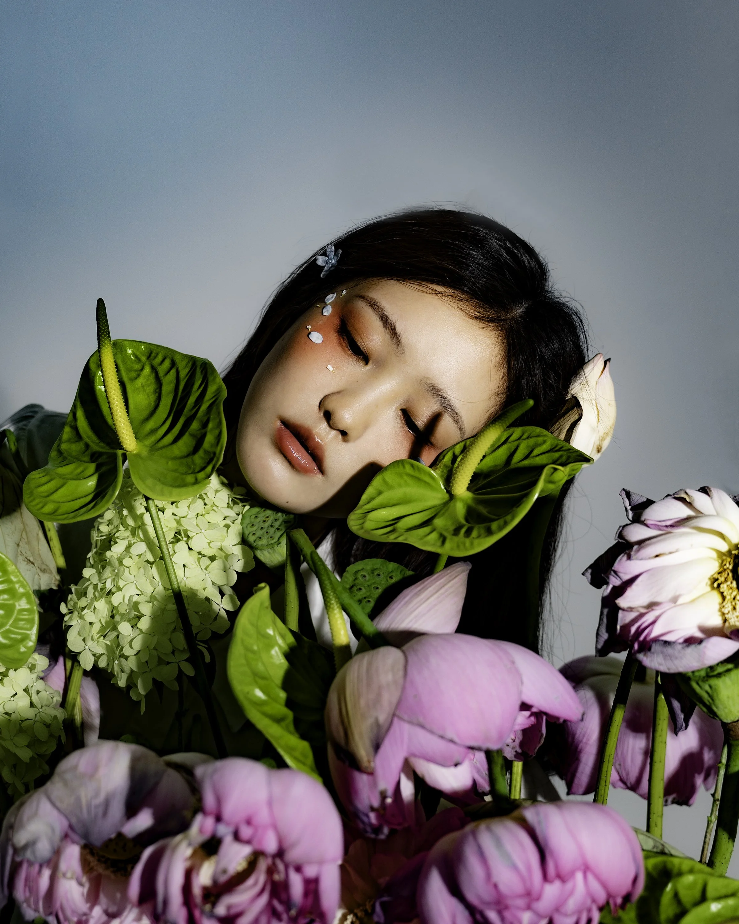 Girl laying her head on flower bouquet, wilting in front, blue background.