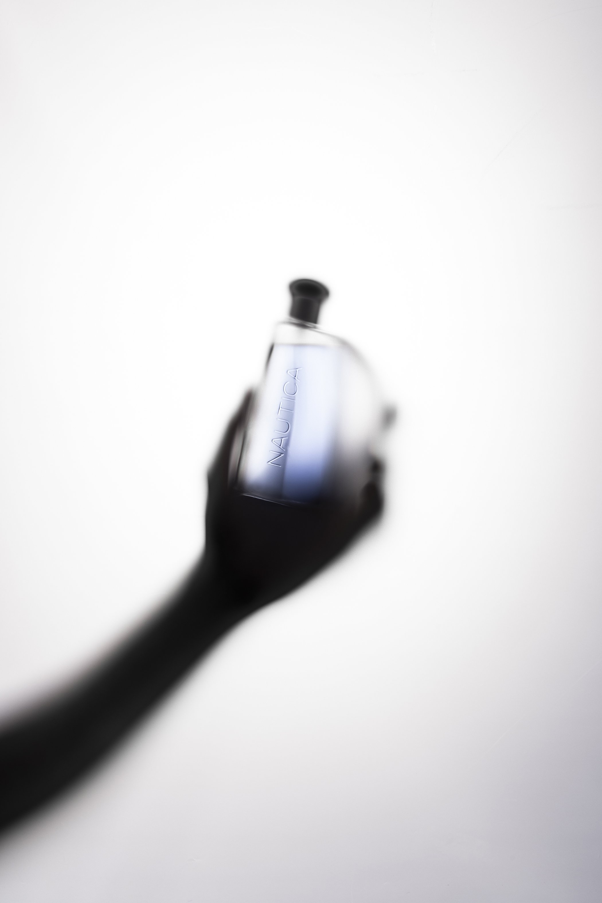 Silhouetted hand holding perfume bottle behind translucent paper, backlit from behind.
