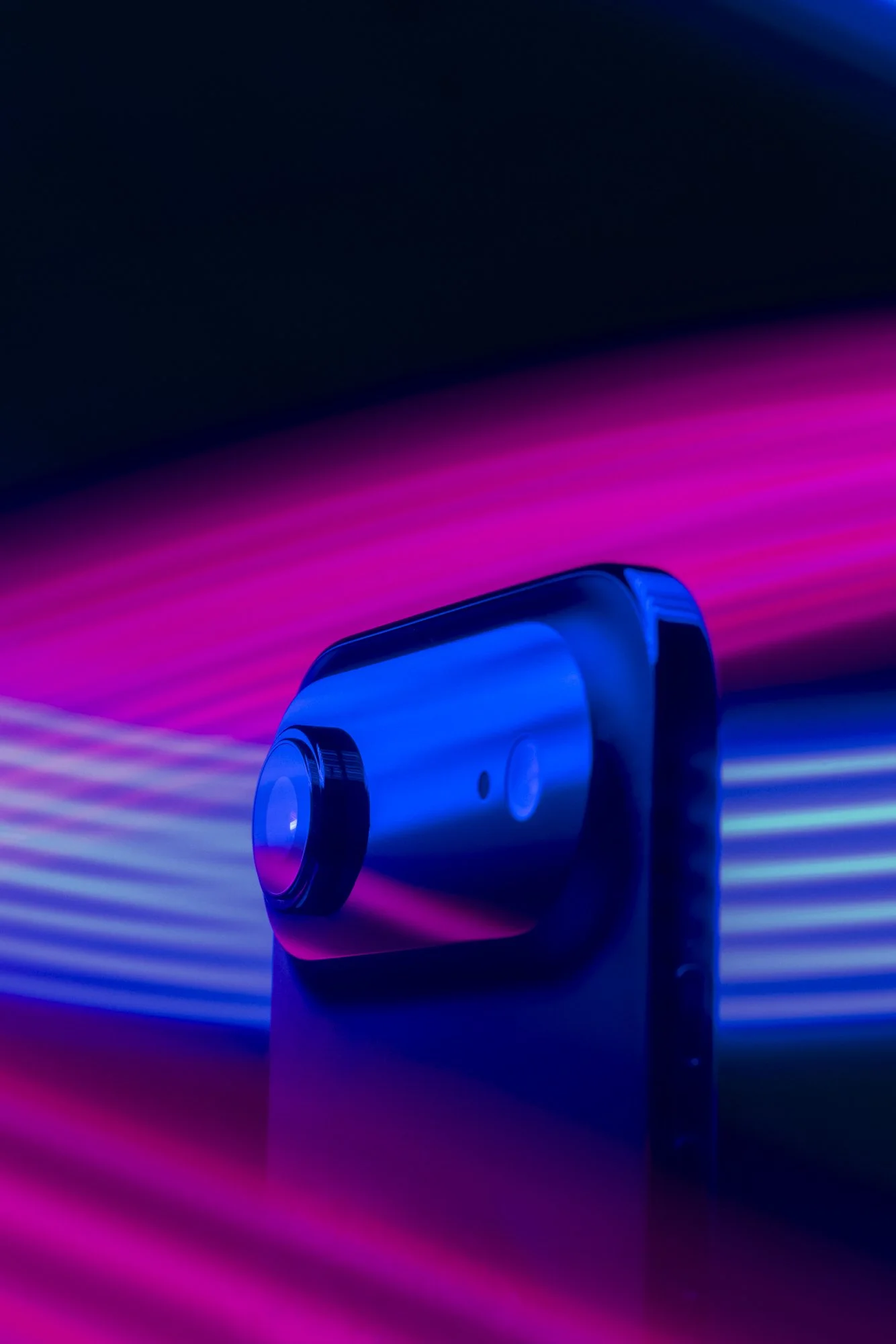 Blue device with lens illuminated by pink and blue light streaks.