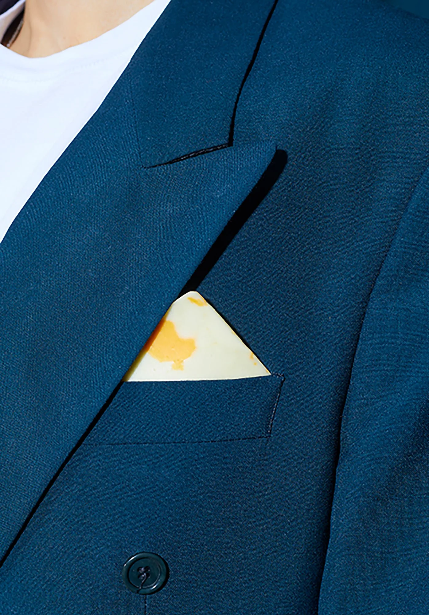 strawberry blonde hair. Closeup of piece of marble cheese in handkerchief pocket of man in navy suit and white t-shirt.
