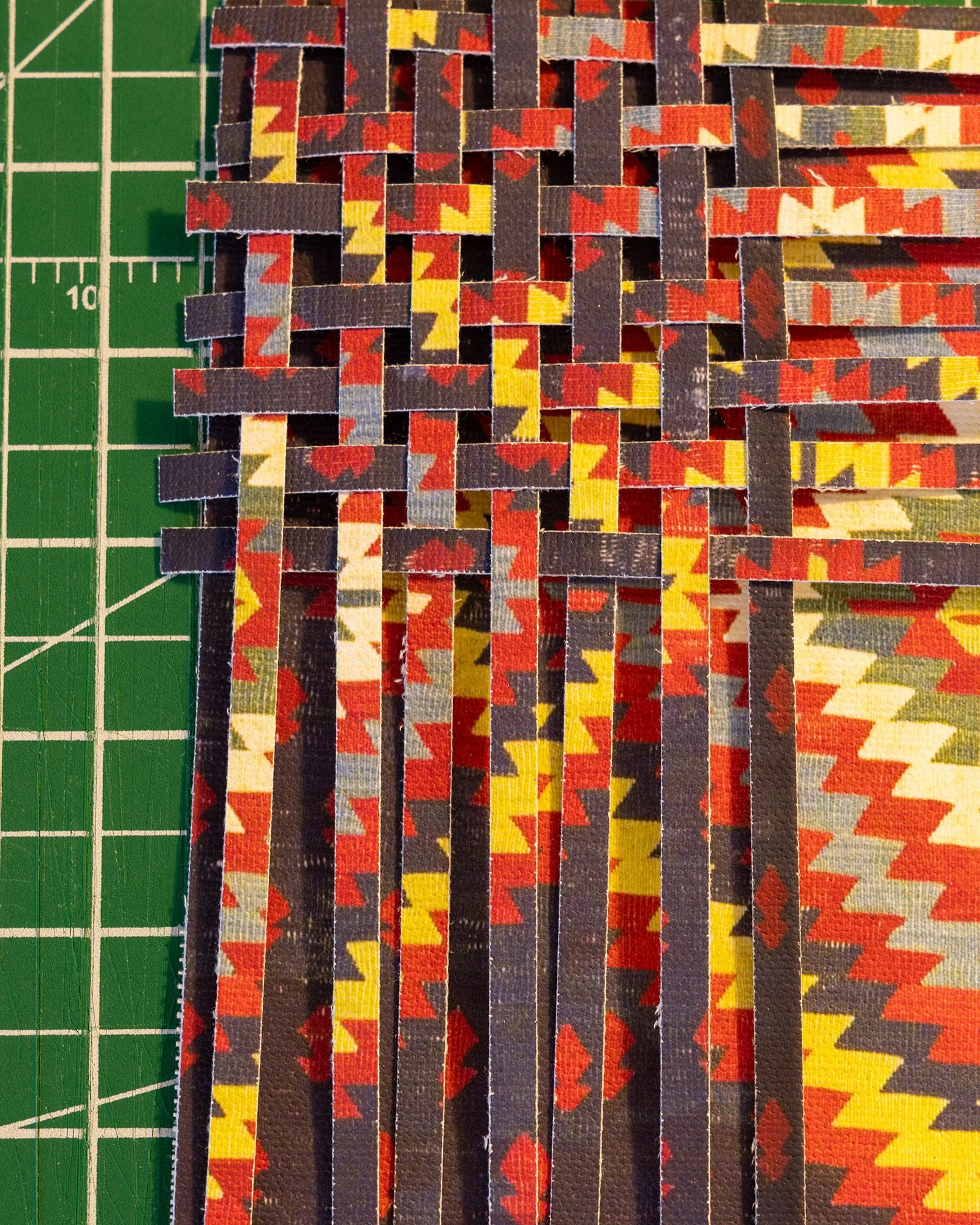 Colourful paper strips with a zigzag pattern are woven together on a green cutting mat.