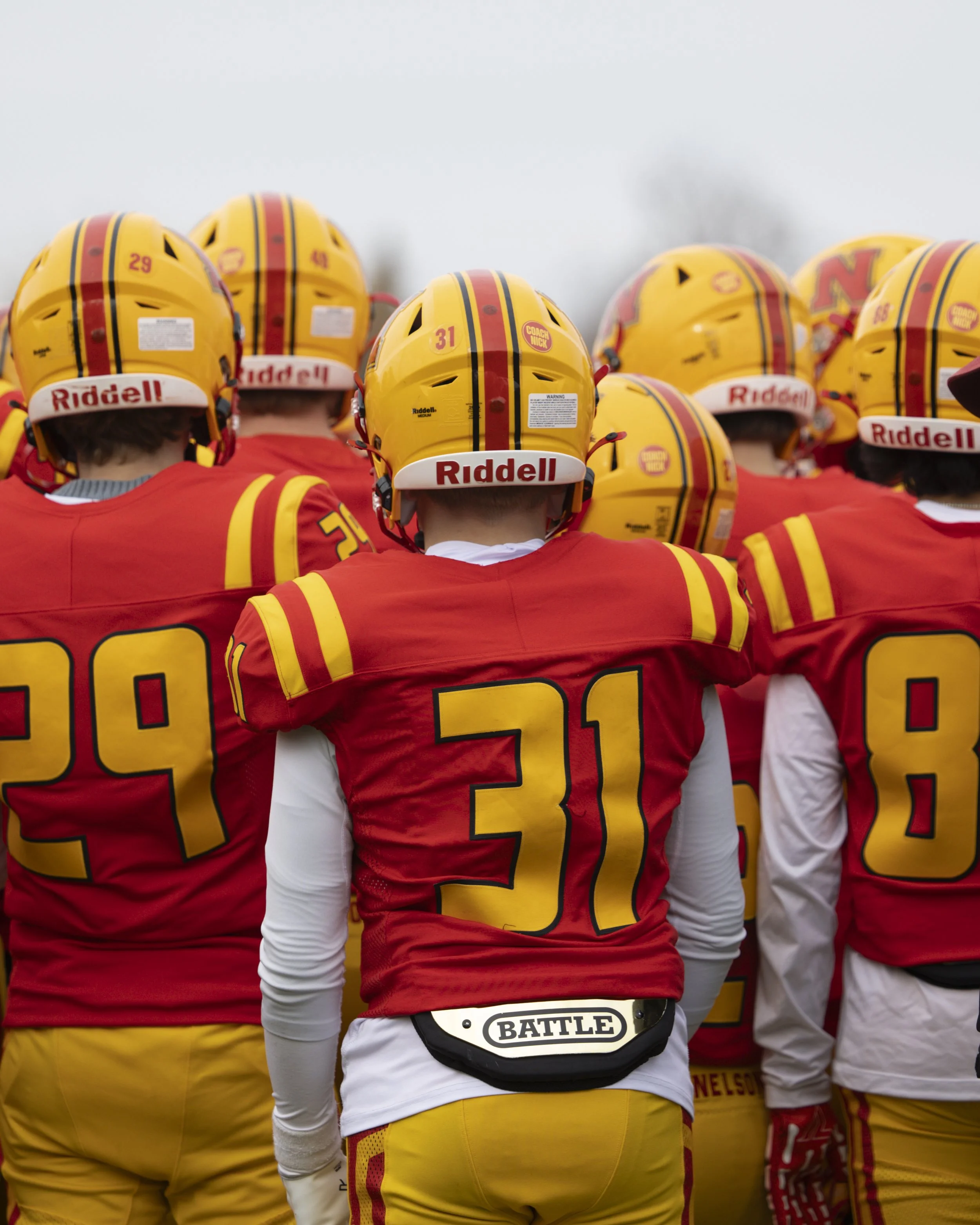 Football player in uniform holding football against body with left arm against red backdrop