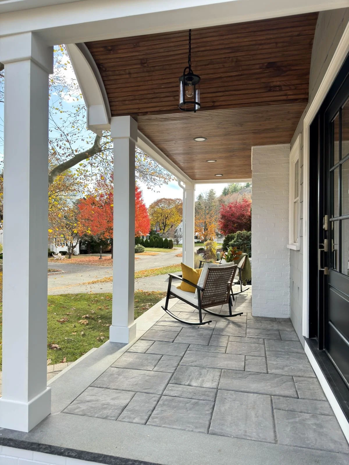 Looking out from the new Melrose covered porch addition, the design captures vibrant New England fall foliage. The arched stained wood ceiling and textured paver floor create a warm, inviting atmosphere for seasonal outdoor living.