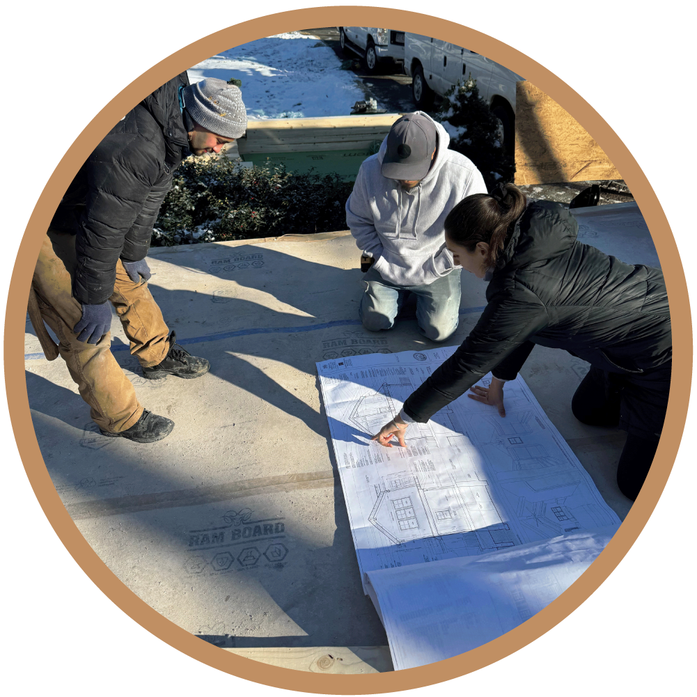 Licensed architect providing construction coordination and architectural oversight in Greater Boston, reviewing architectural plans on-site with a framing crew.