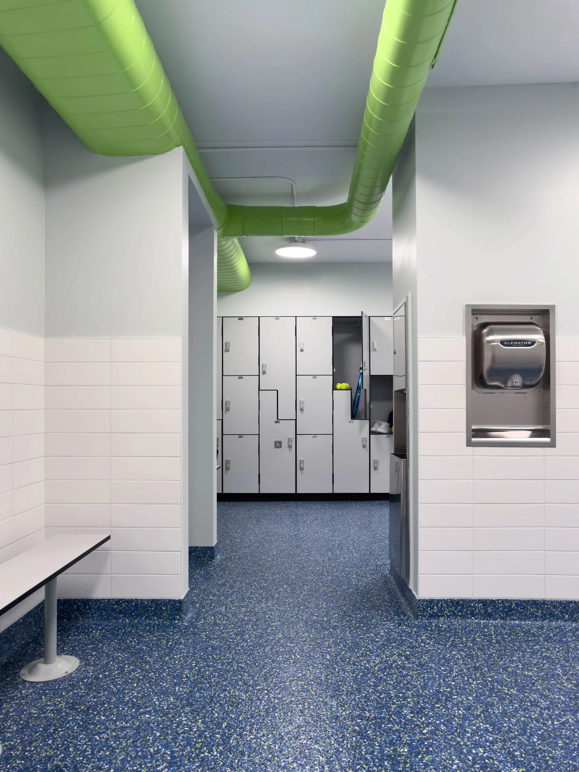 women's locker room entry view with green exposed ductwork, stainless hand dryer and grey lockers in the distance