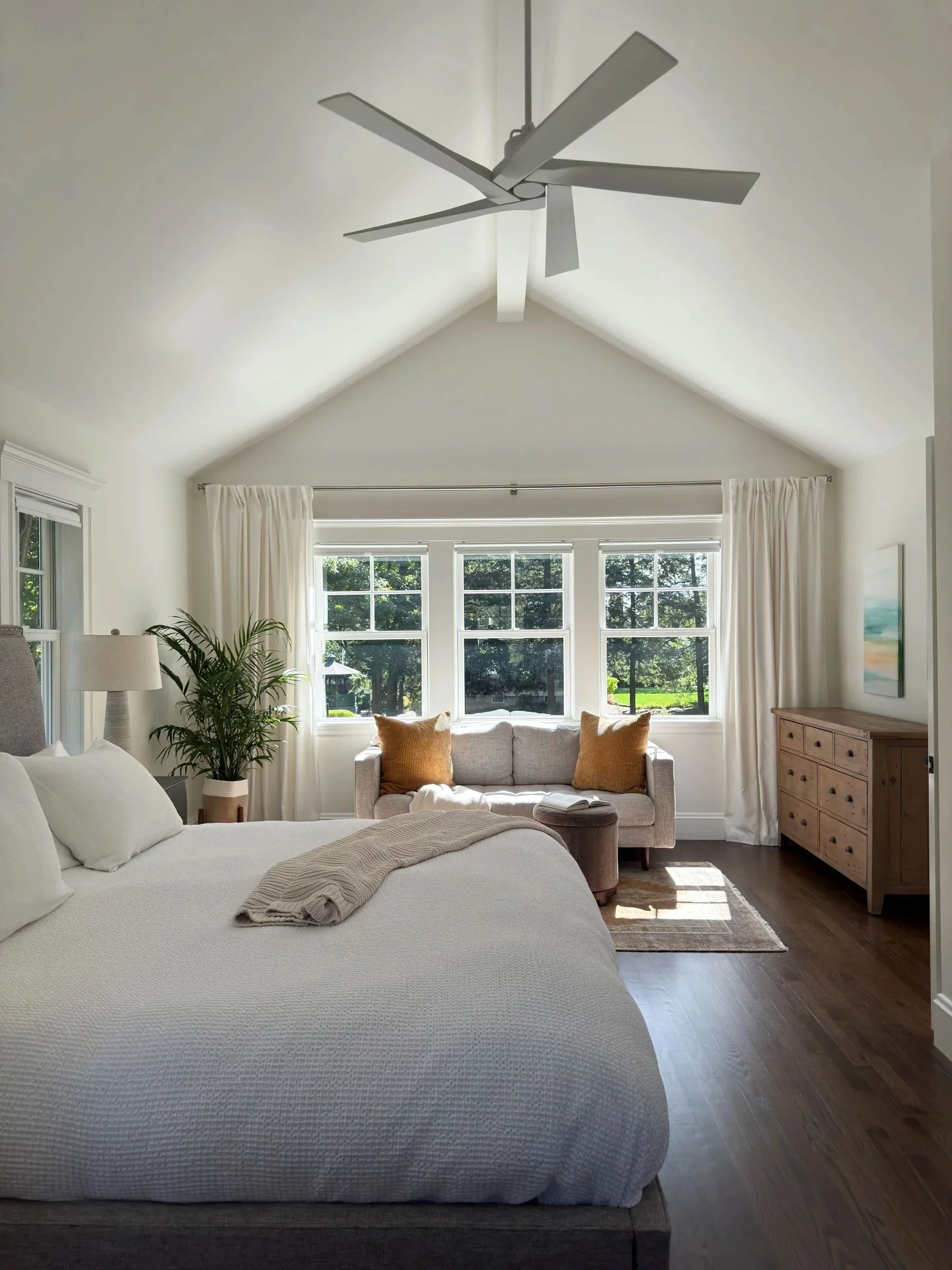 Completed vaulted primary suite addition in Greater Boston showing king bed, vaulted ceiling, reading lounge and triple window array designed by Tact and Grit Design Co.