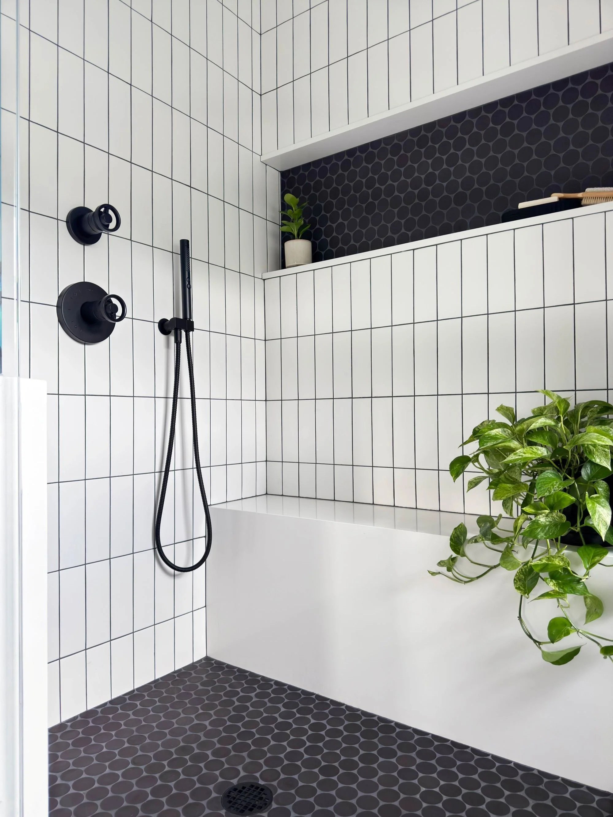 Modern primary bath walk-in-shower with waterfall stone bench and horizontal continuous shampoo niche with large circular mosaic tile and vertically stacked subway walls