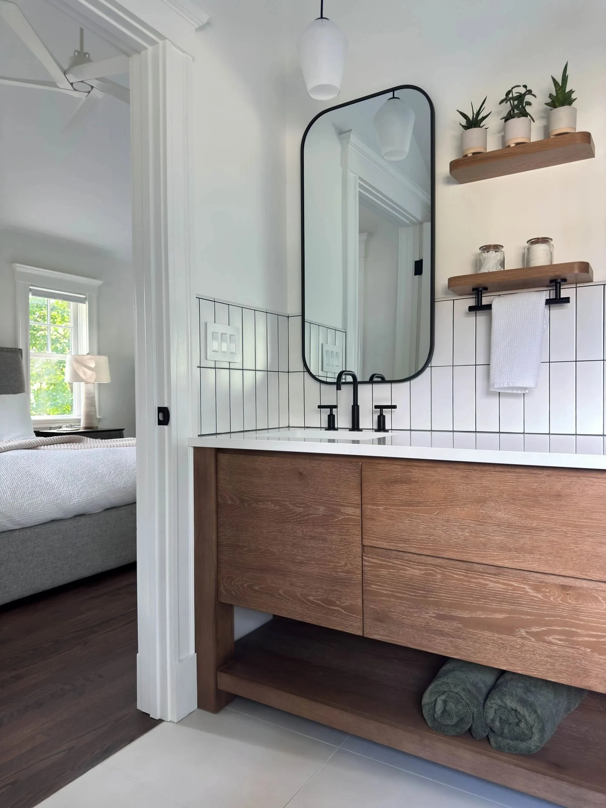 Built-in double vanity featuring black fixtures and floating shelves with door open viewing primary bedroom beyond 