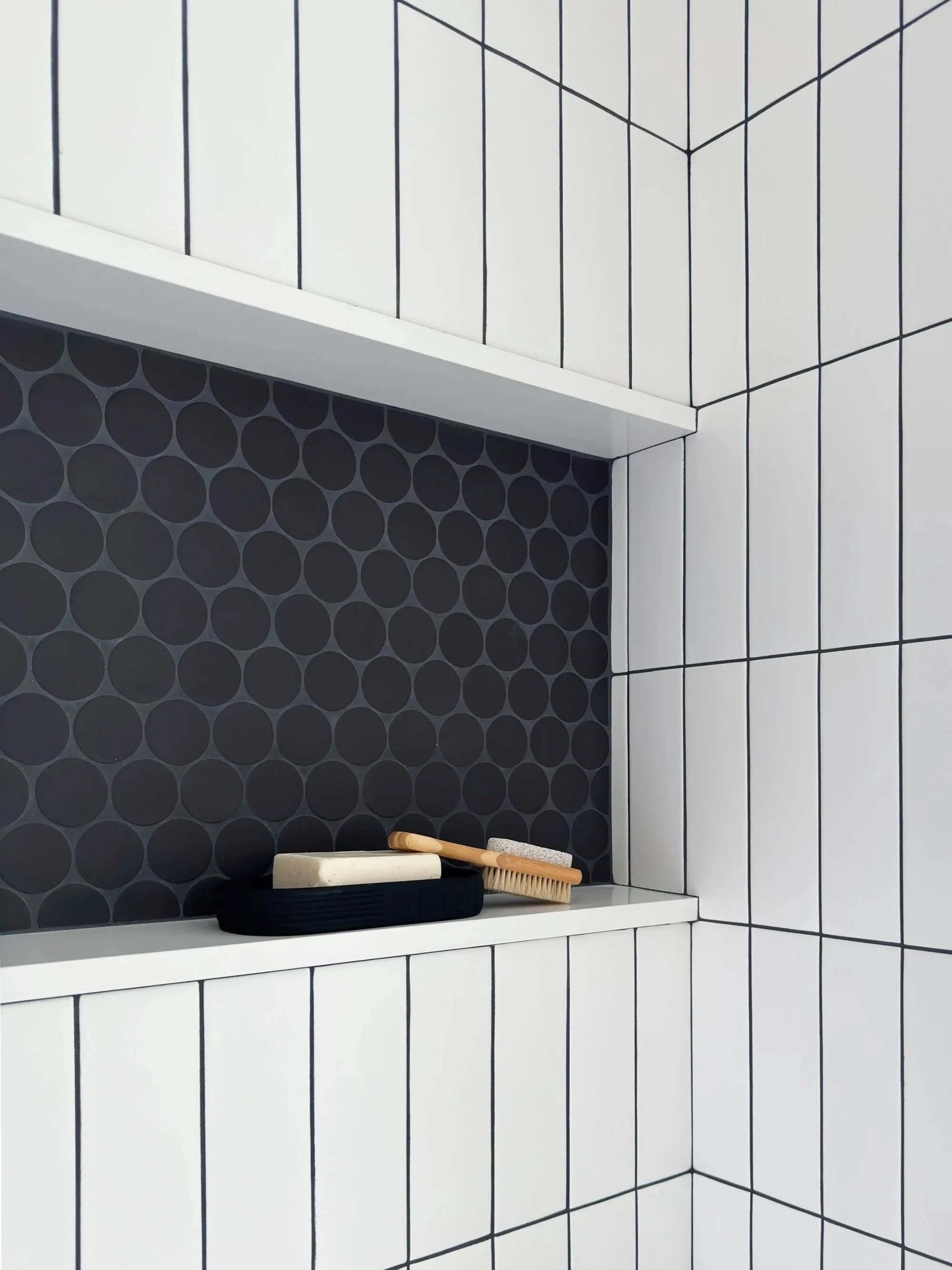 Primary bathroom modern shower niche detail depicting horizontal continuous niche with large circular mosaic tile backsplash as it meets the stacked white subway tile