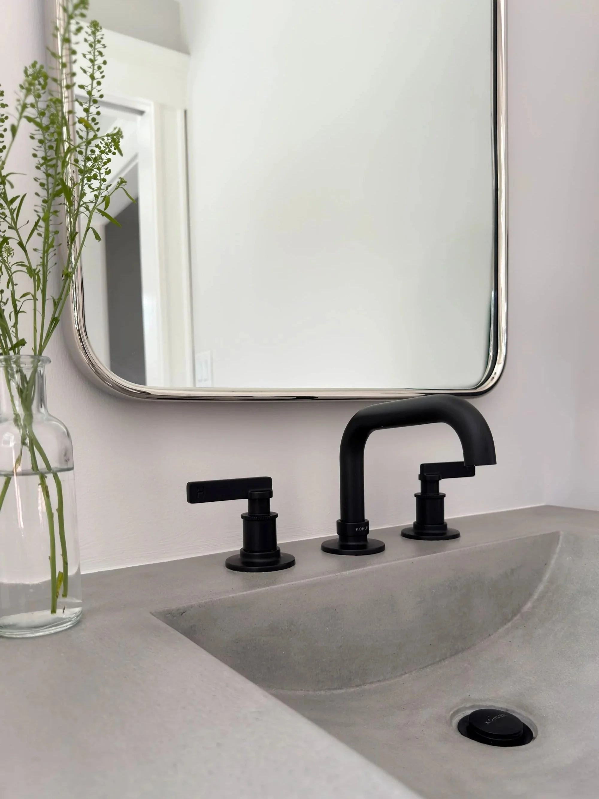 detail of concrete integrated countertop and sink with black Kohler widespread faucet and polished nickel mirror