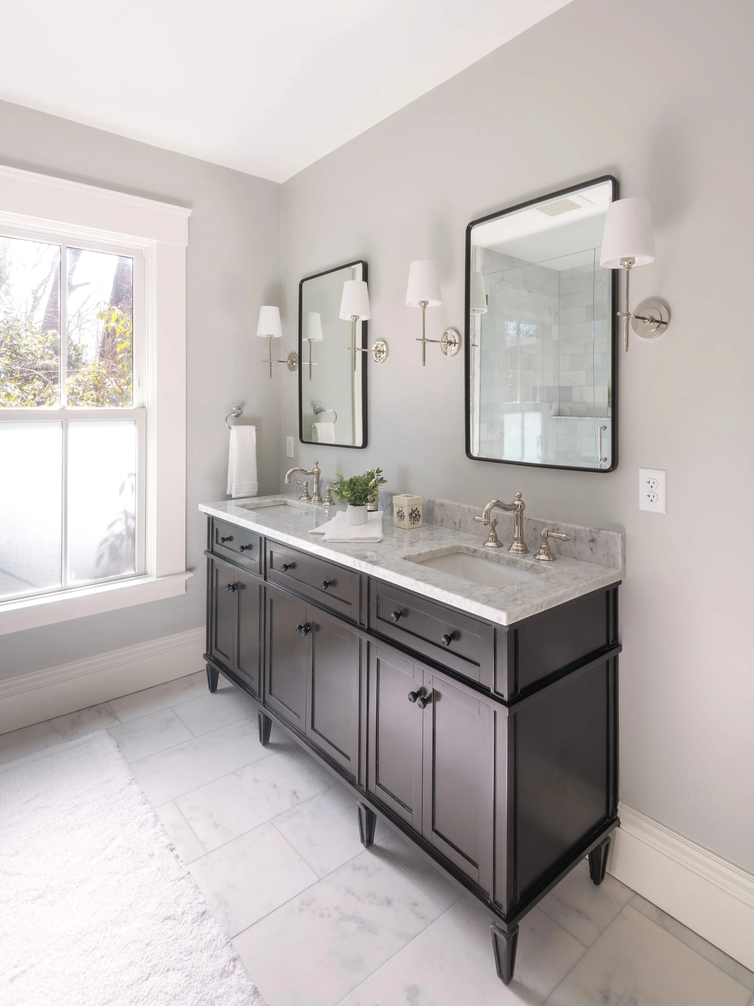 Renovated primary bathroom vanity of an 1846 Victorian home in Newton MA featuring black traditional double vanity with marble countertop, polished nickel fixtures and rectangular mirrors