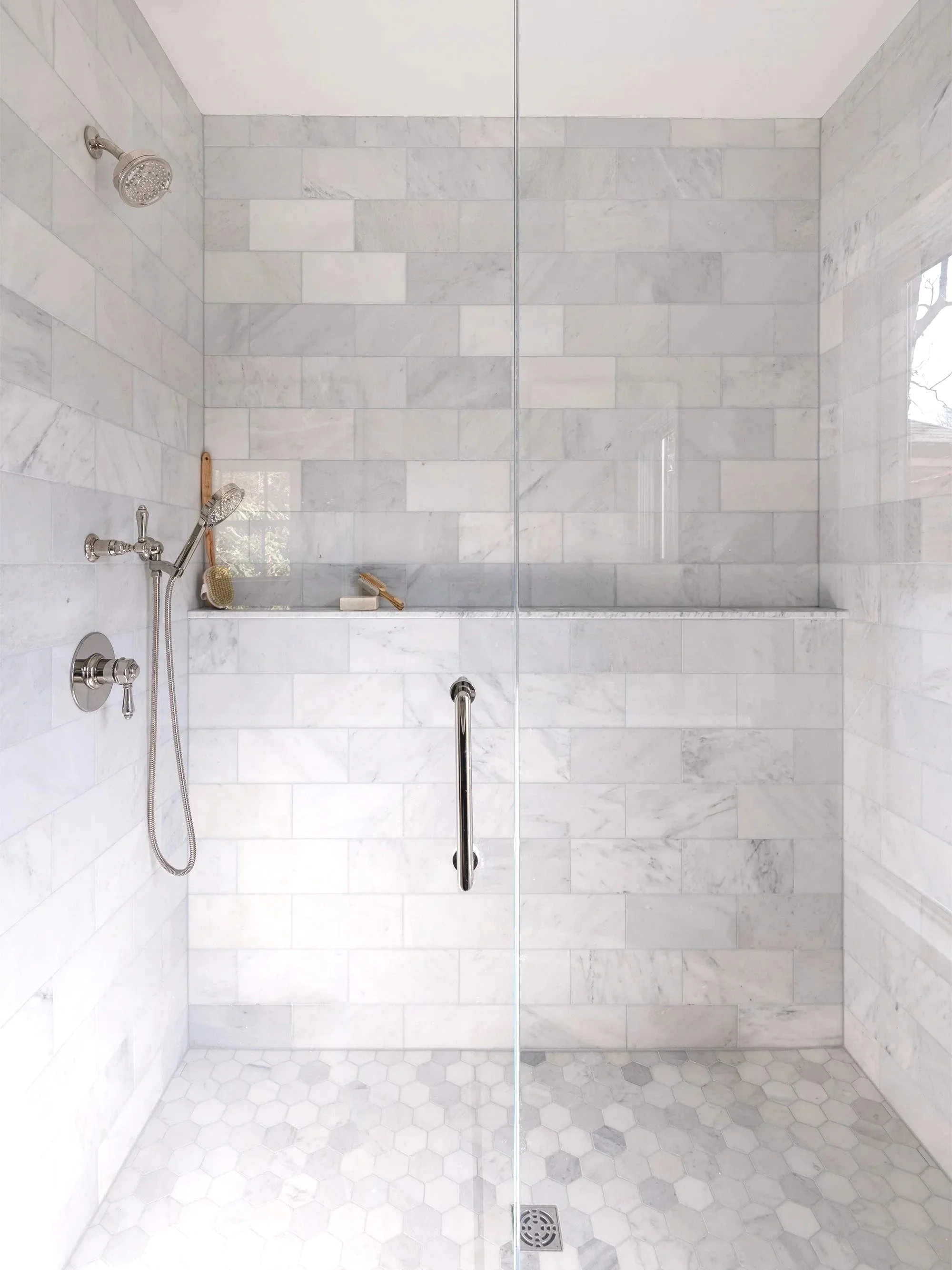 Renovated primary bathroom shower of an 1846 Victorian home in Newton MA featuring floor to ceiling marble tile, polished nickel fixtures and built-in shower ledge