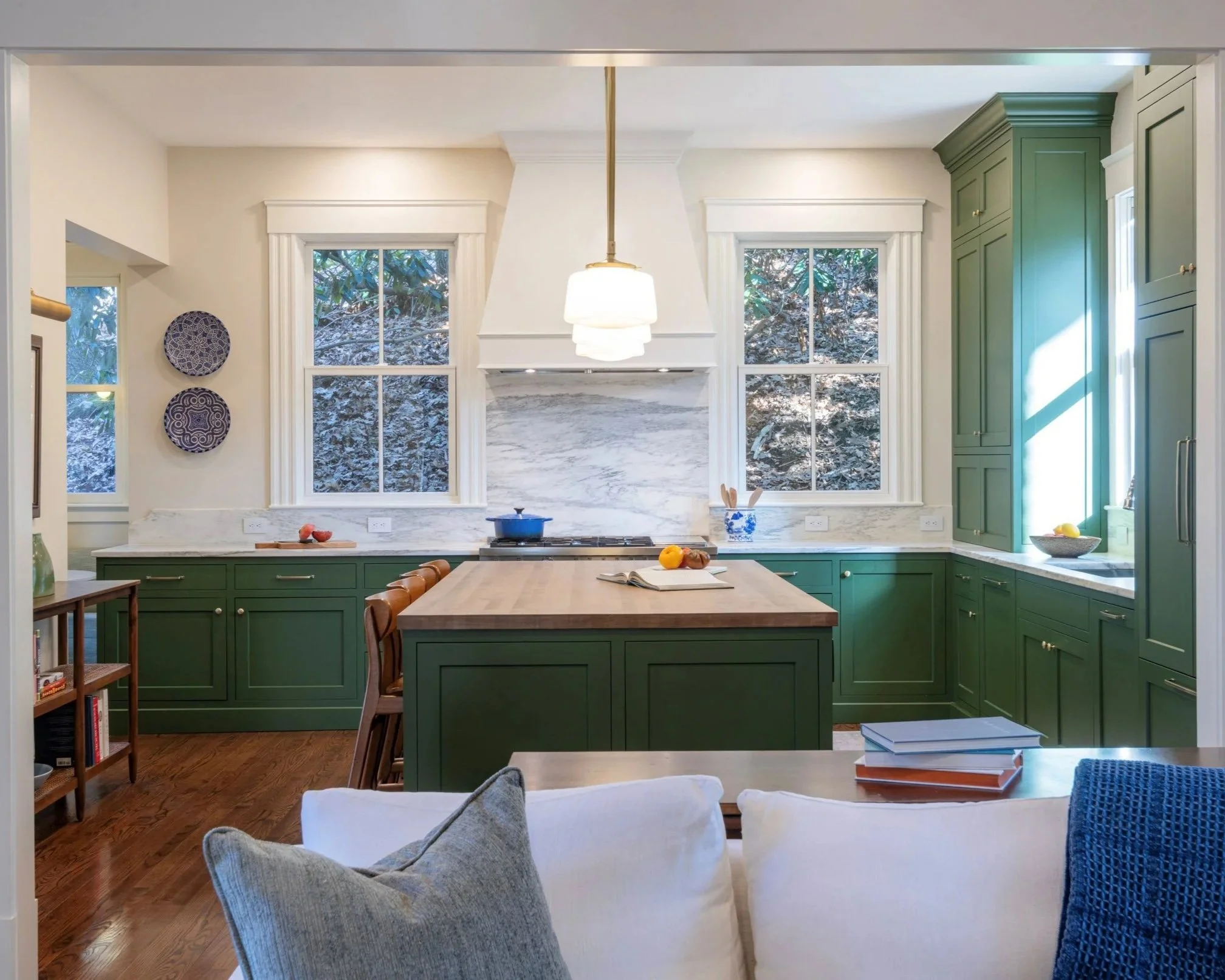 View of green kitchen cabinetry with butcher block island and custom white range hood from new den following removal of chimney and partition.
