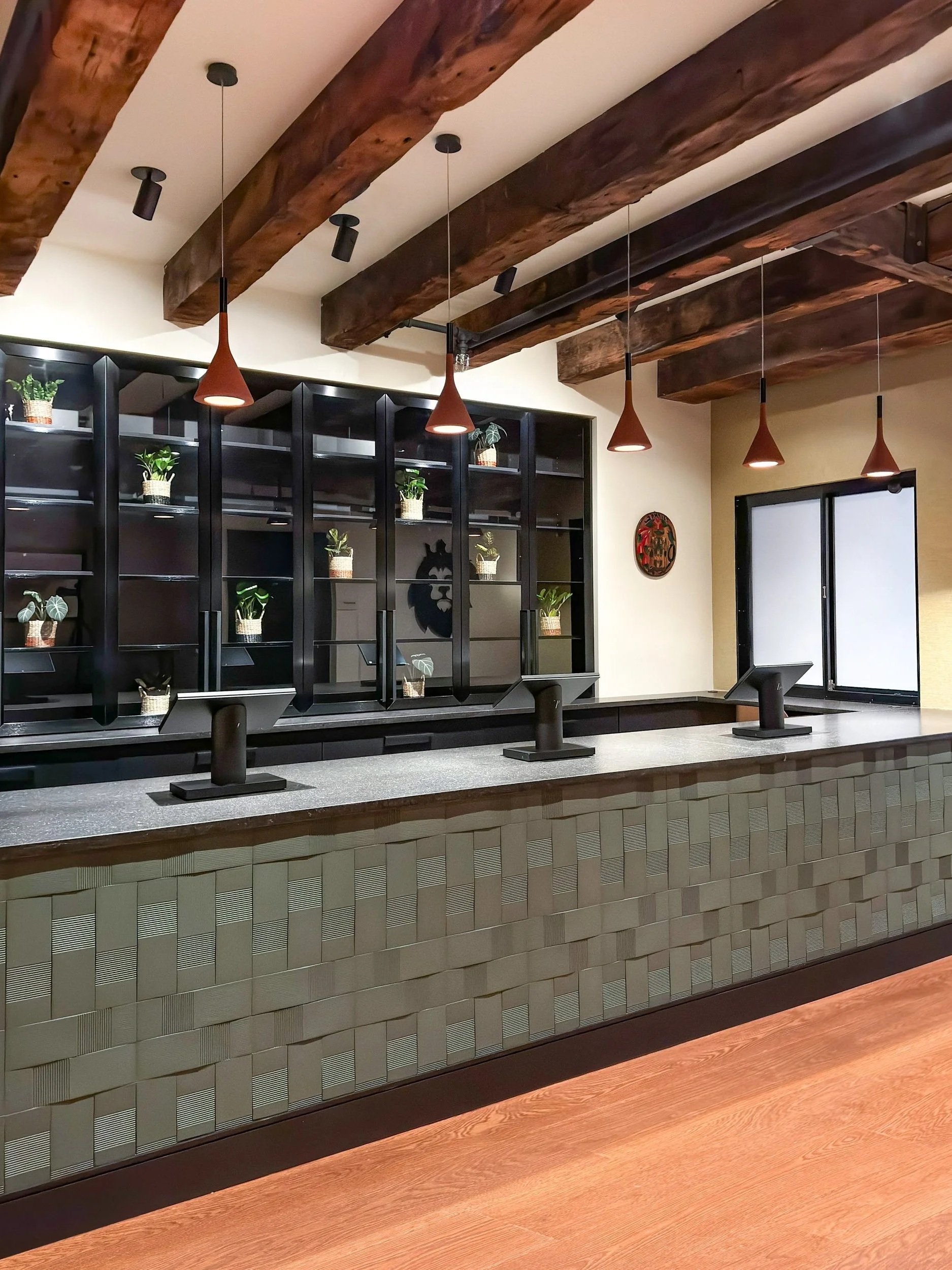Textured green tile faced cash wrap with large black and glass custom displays behind the counter and heavy timber beams above.