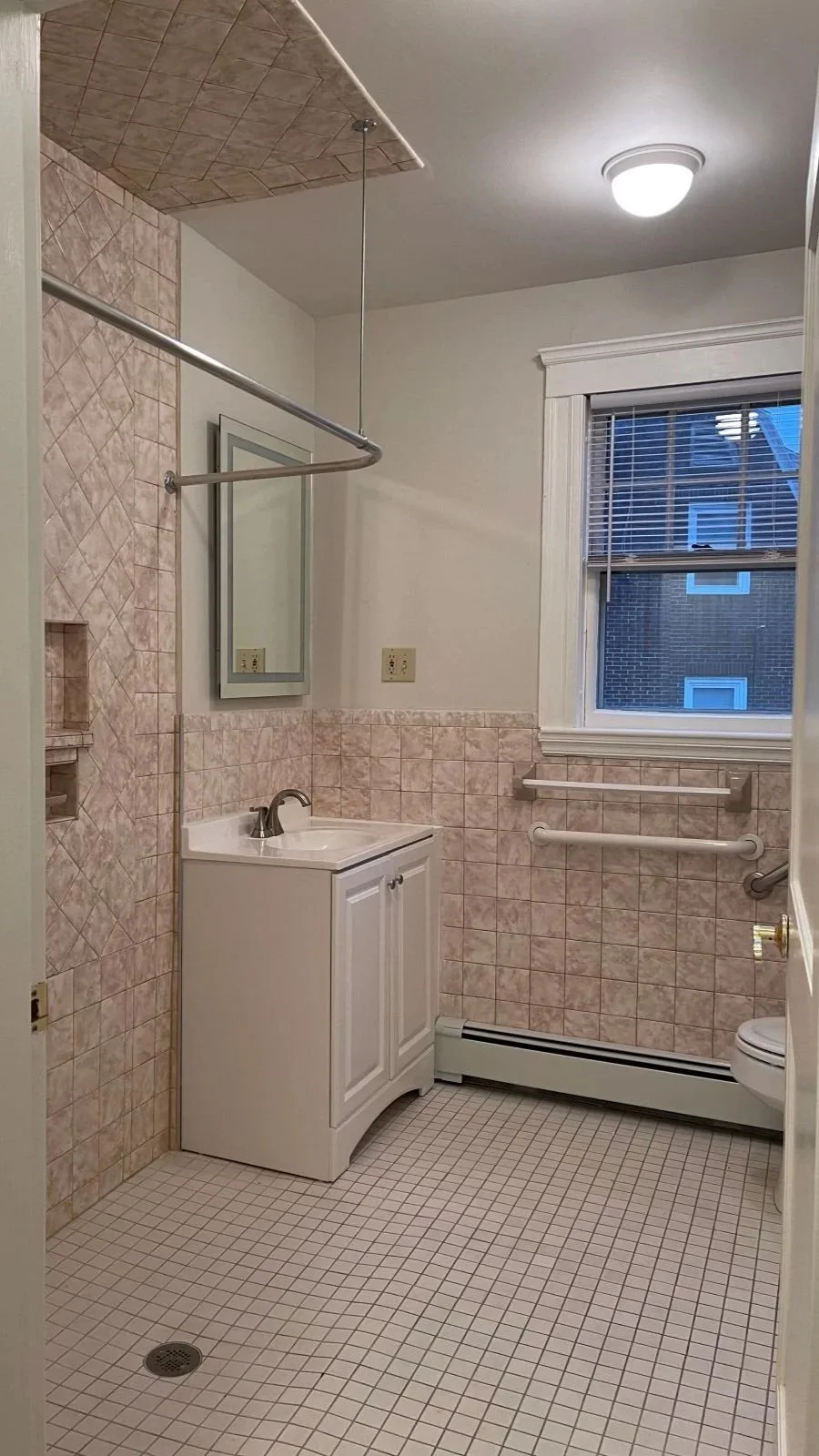 Antique pink tiled bathroom with roll in shower and small vanity.