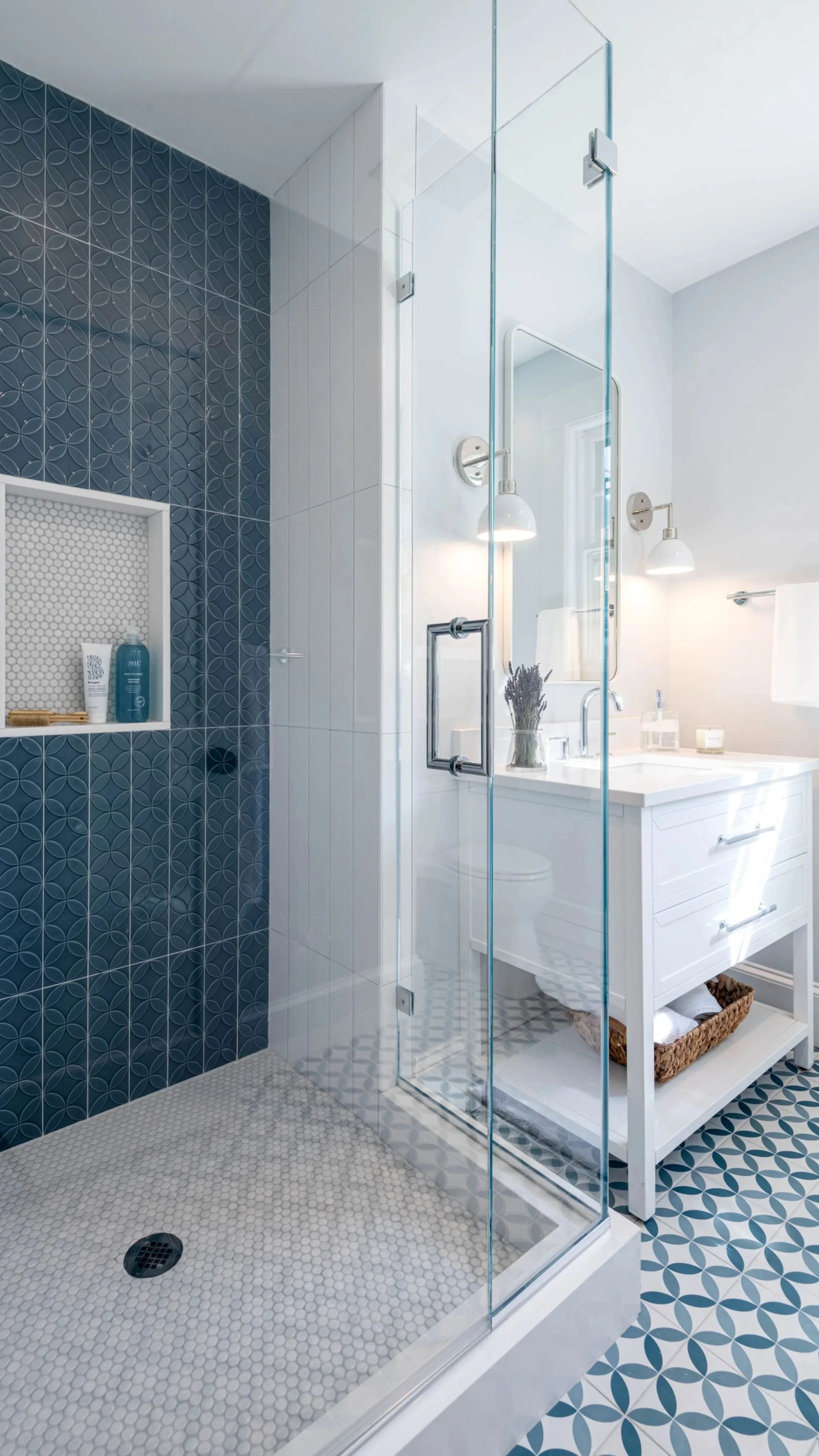 Blue and white tiled bathroom with custom shower, shampoo niche and white vanity with sconces and mirror above.