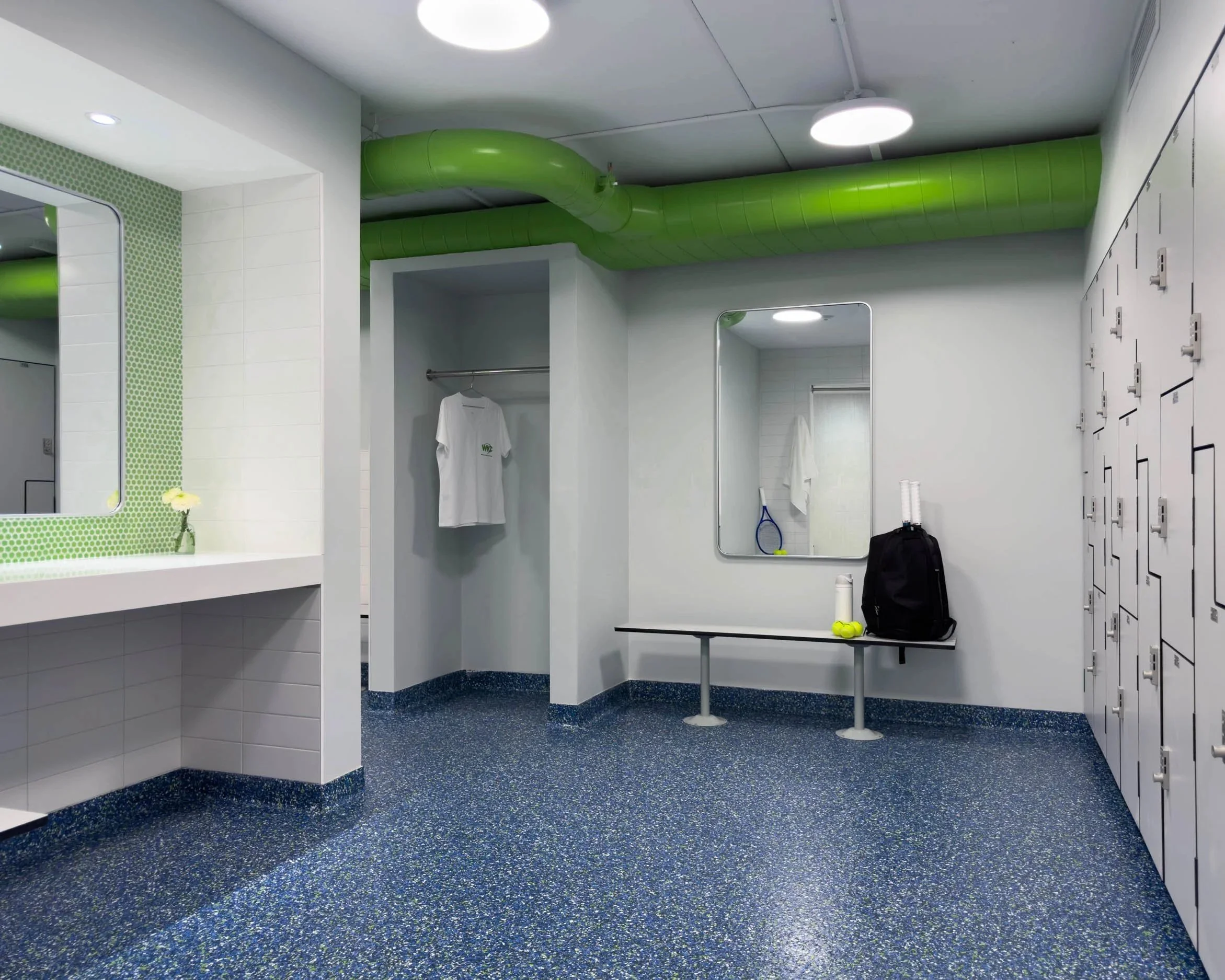 Changing area in newly renovated locker room with built-in lockers and integrated locks, make-up vanity and benches in a blue, green and gray color palette.