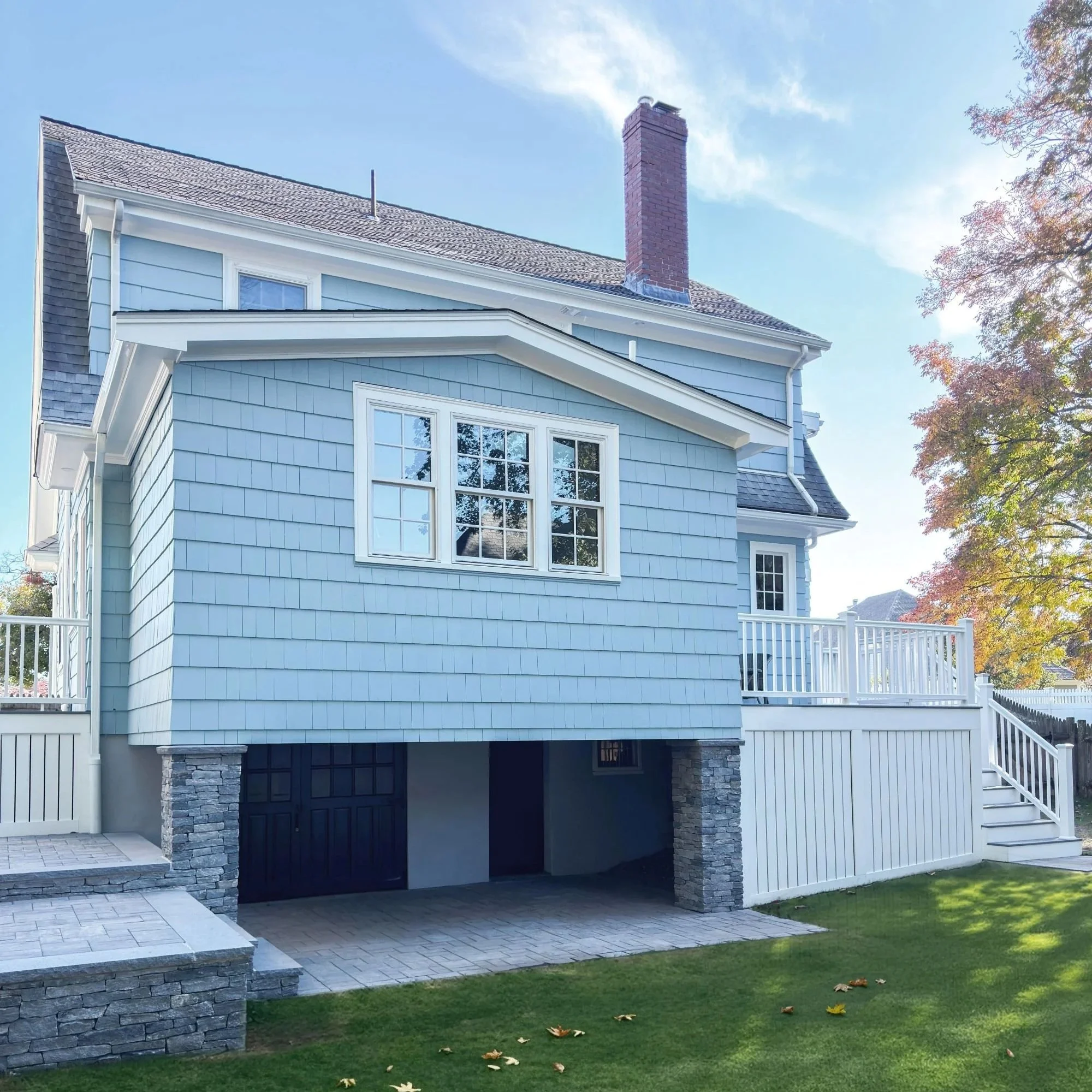 Blue exterior kitchen addition with triple windows and gable roof with a patio and deck flanking both sides.
