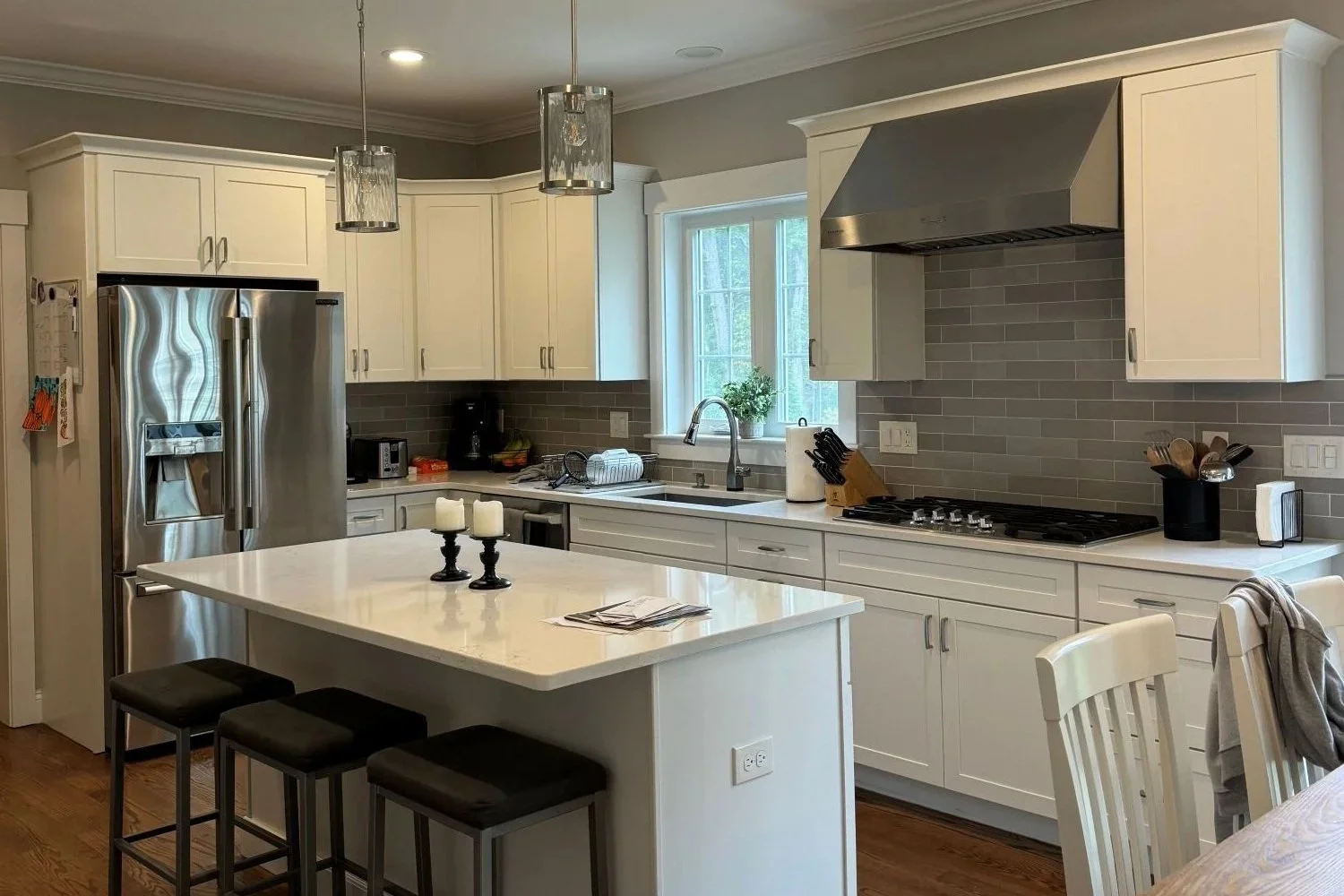 A white kitchen with stainless steel appliances and brushed nickel and glass pendant lights over island.