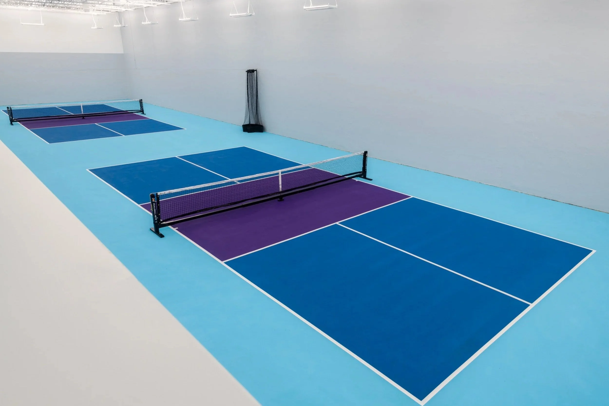 Aqua, navy and purpled colored pickleball courts with gray walls in an indoor athletic facility.