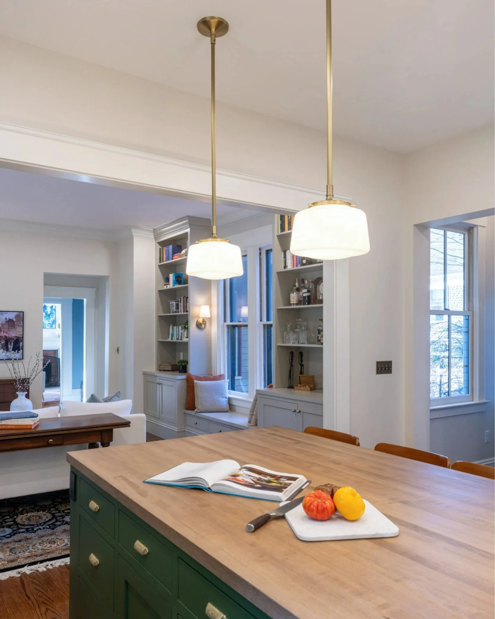 Large butcher block island with pendants and custom library shelving beyond following removal of chimney and partition.