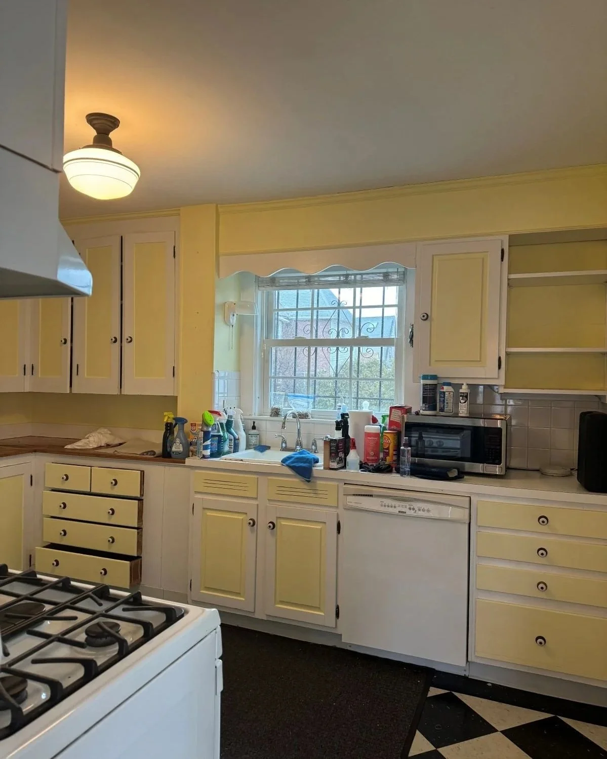 Original, dark early 1900's kitchen painted yellow and white with small sink window over sink.