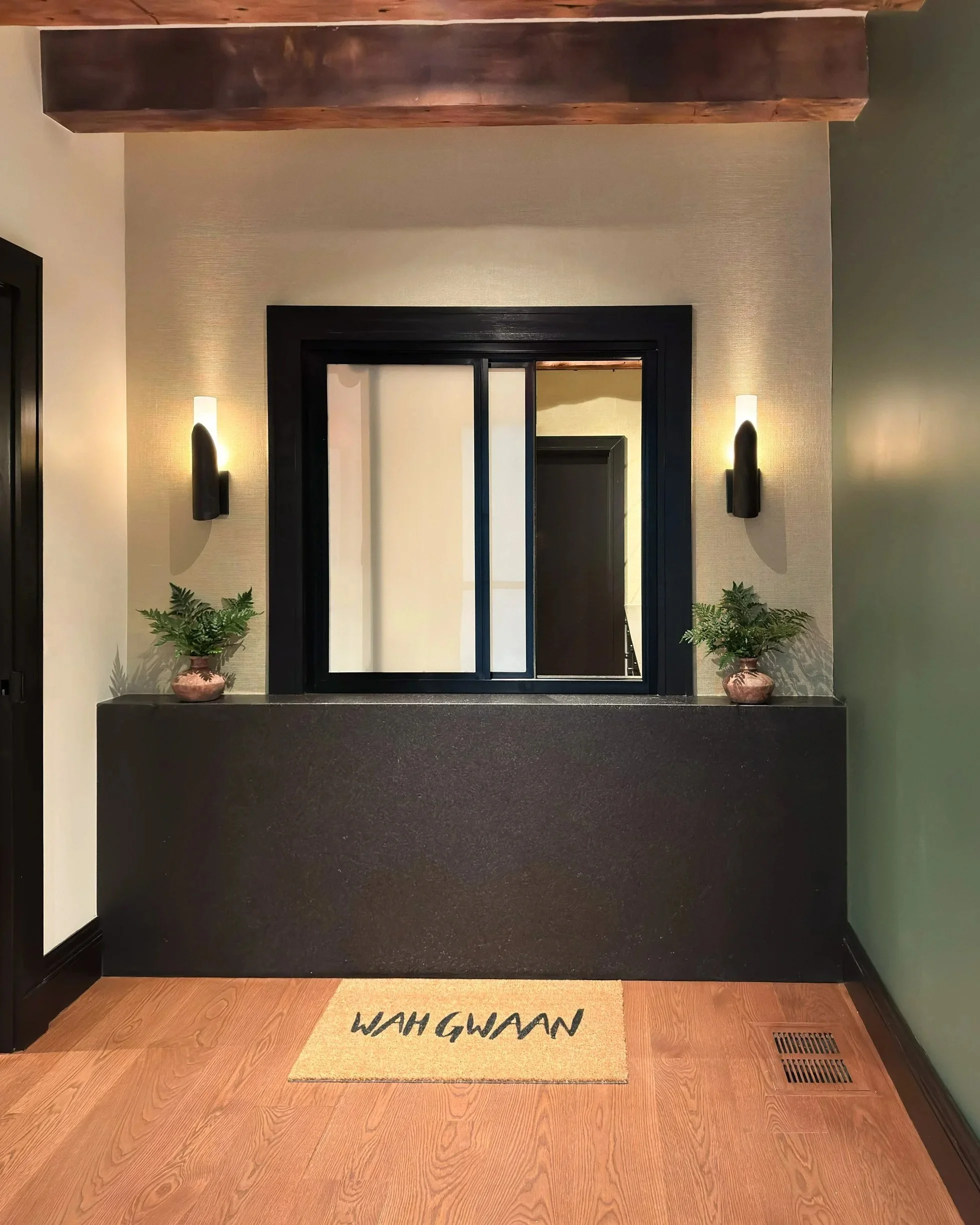 Warmly lit entry vestibule with exposed heavy timber beams, a waterfall granite check-in counter and sliding window.