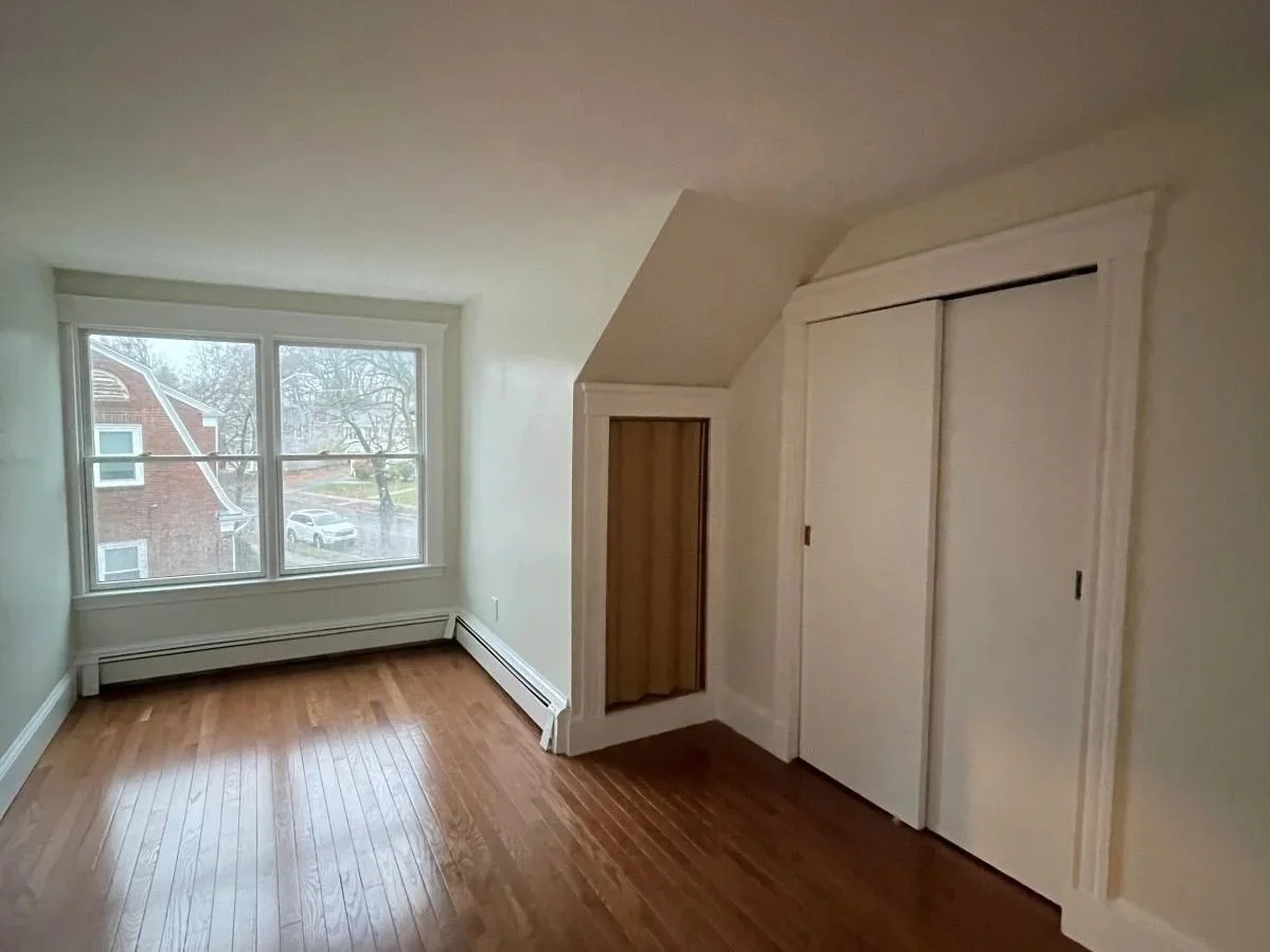 Empty bedroom with amber floors, sliding doors to closet and double hung windows.