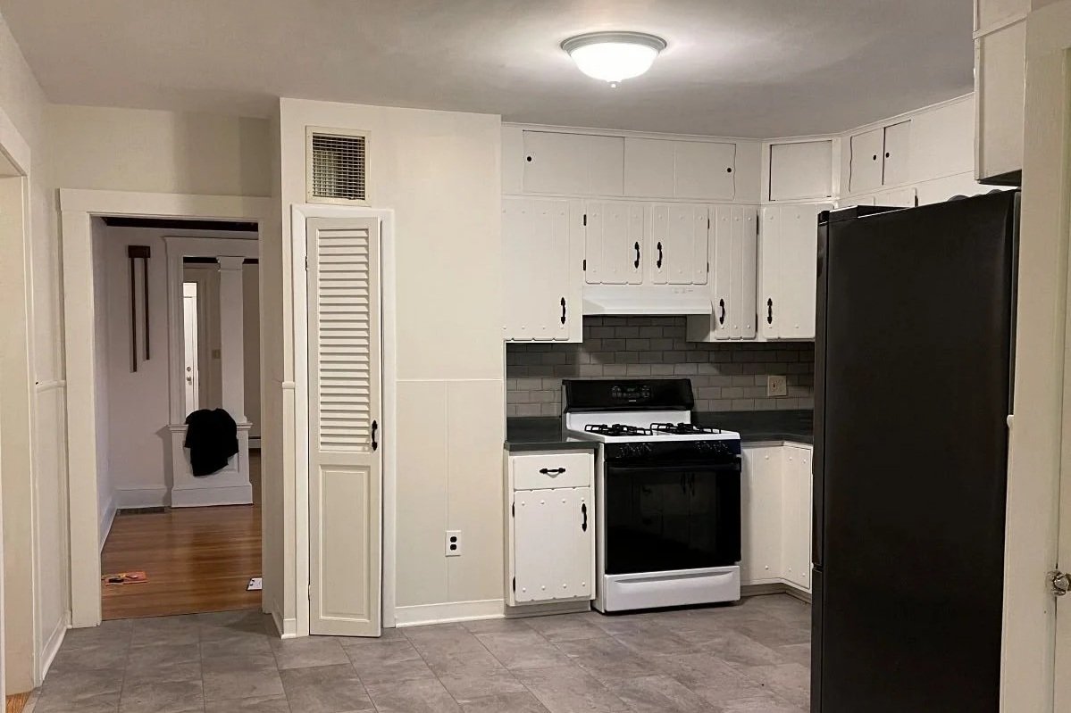 Dated kitchen with white cabinetry, old appliances and linoleum floor with small cased opening to dining room.