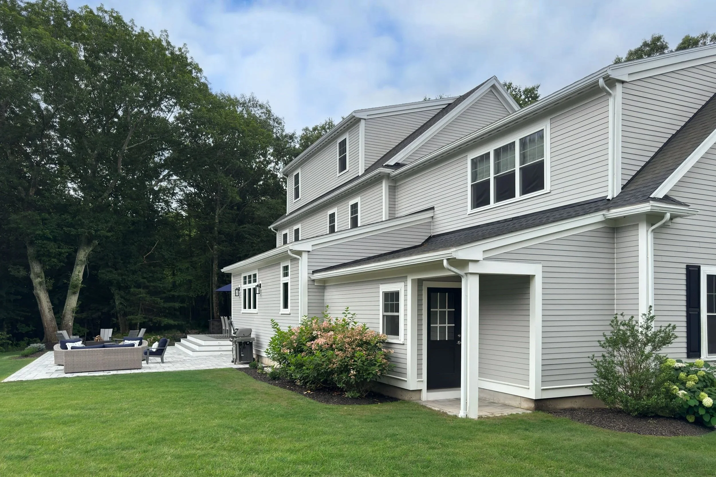Side view of the home expansion showing the rear entry way to the fully enclosed basement stair and garage expansion with the patio seating area beyond.