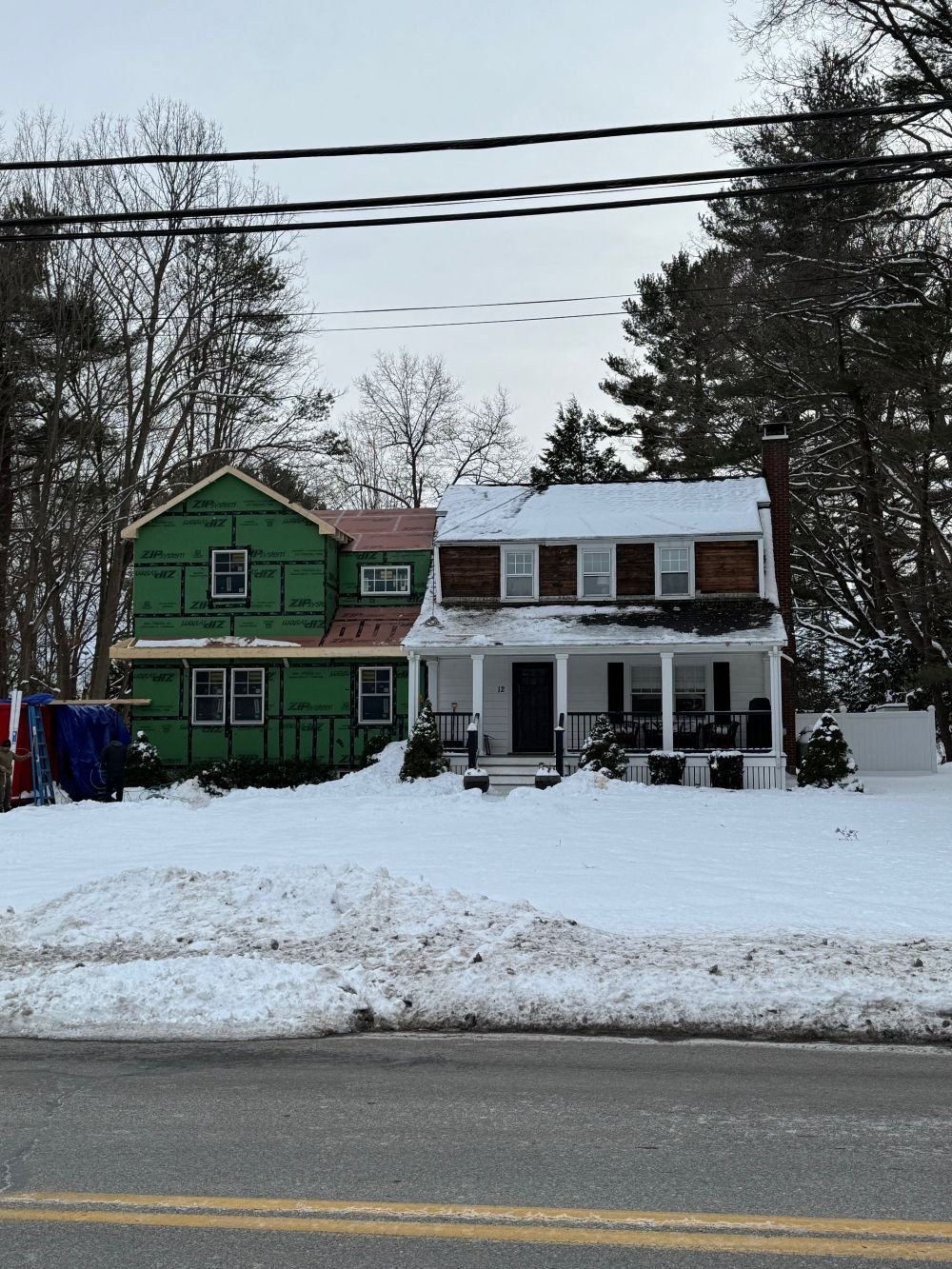Exterior enclosure phase of a Dutch Colonial second story addition in Greater Boston showing wrapped building envelope during winter construction designed by Tact and Grit Design Co.