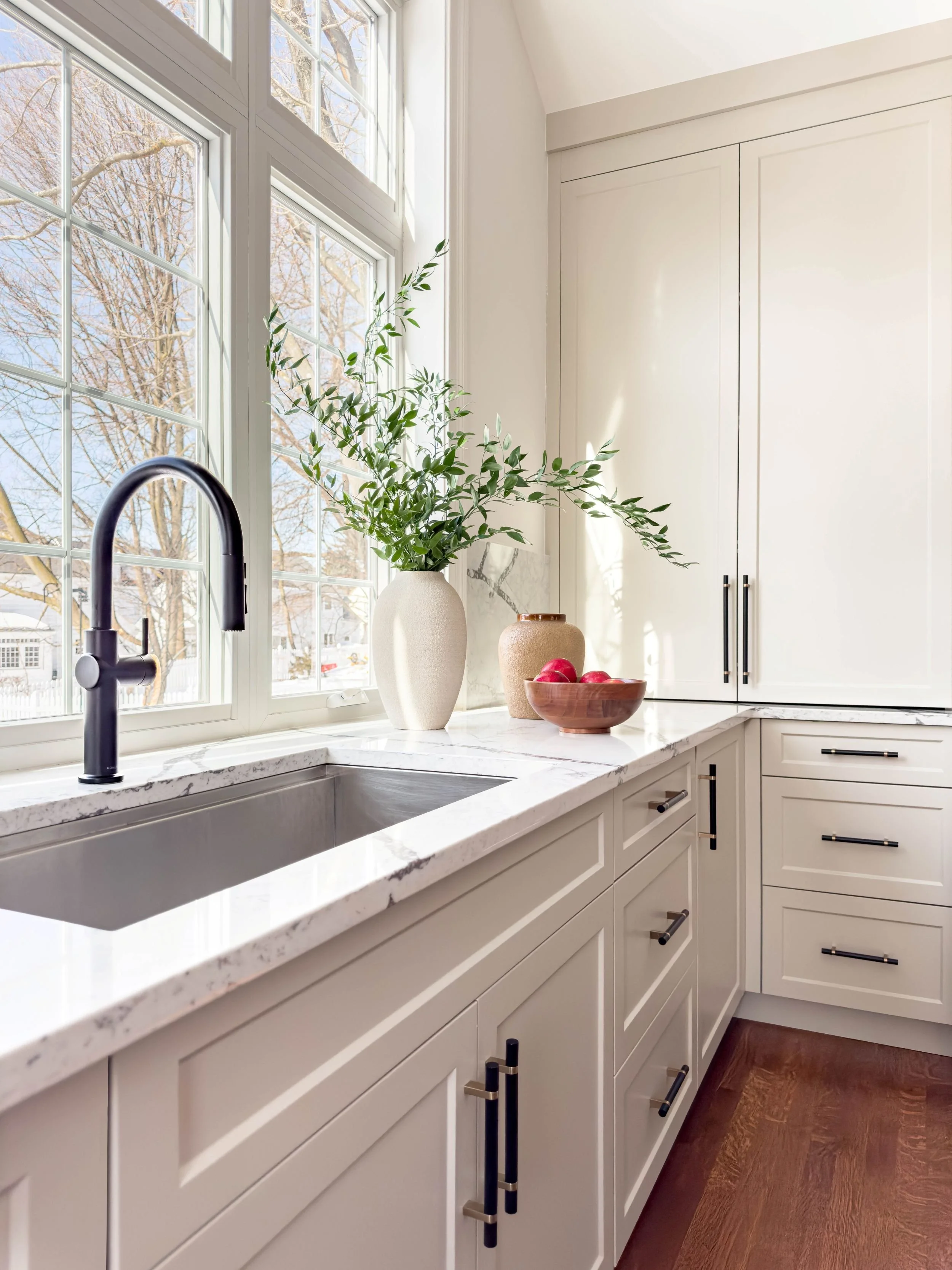 Transitional kitchen sink area featuring a massive picture window . The marble-style quartz countertop extends directly into the window sill for a seamless, continuous surface perfect for plants or herbs. 