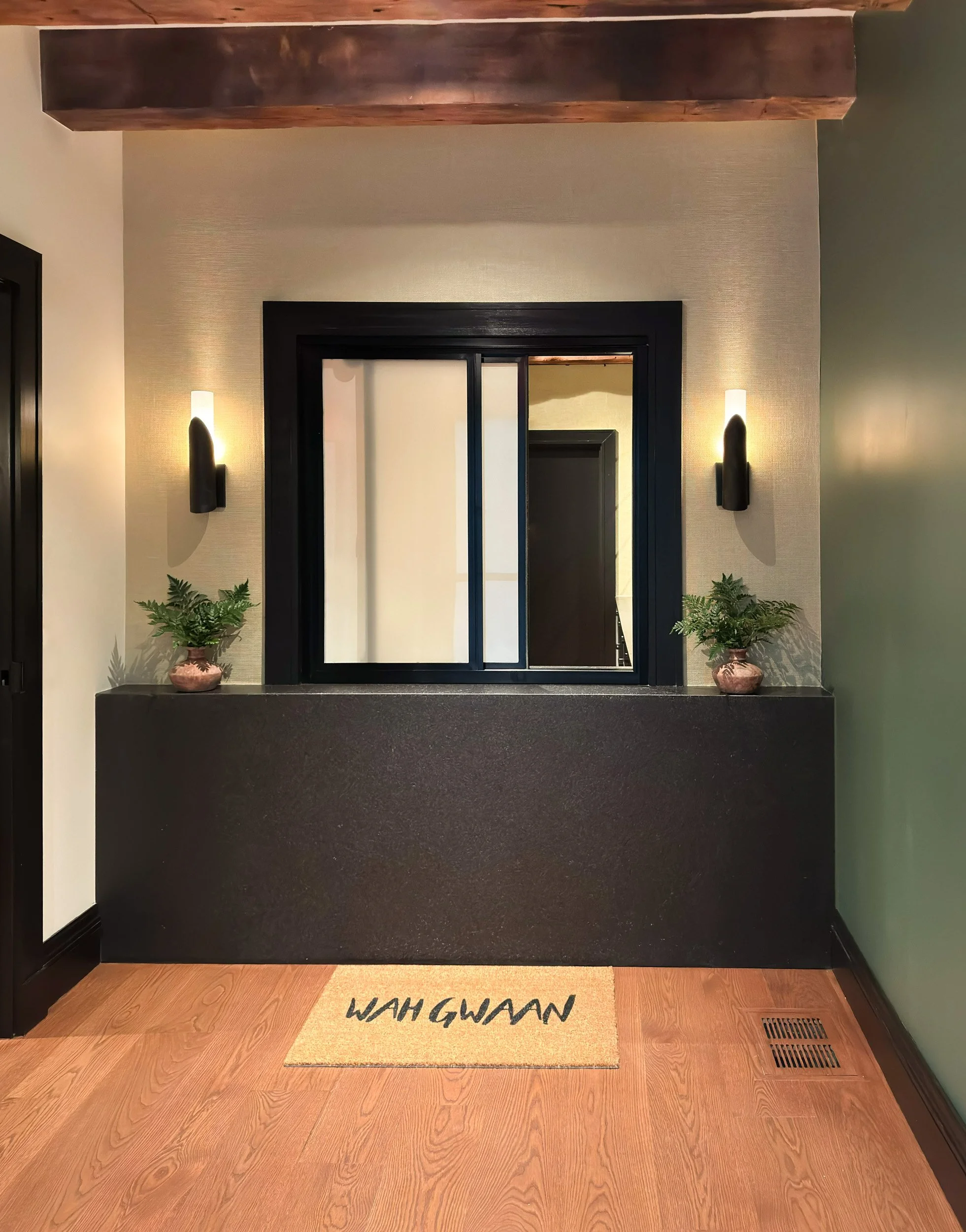 Black granite waterfall check in counter with sliding transaction window, gold texture wall covering, terracotta vases with ferns and black wall sconces.