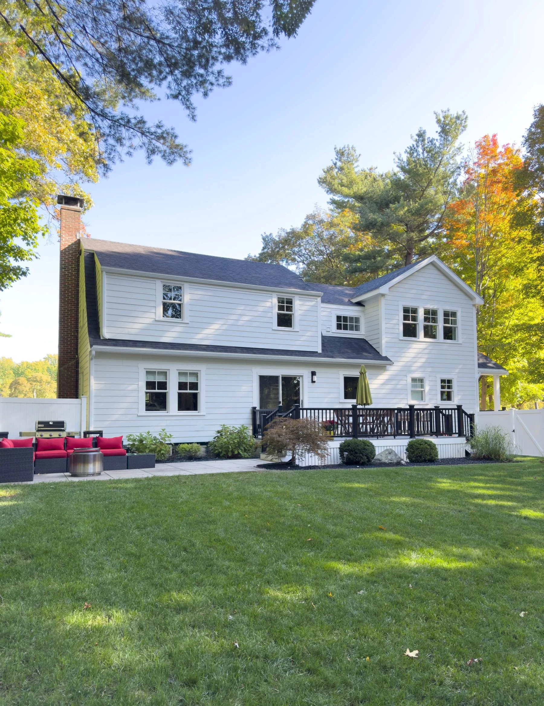 Completed rear exterior of a Dutch Colonial second story addition in Greater Boston showing new Hardie siding, Marvin windows, rear patio and second story addition by Tact and Grit Design Co.