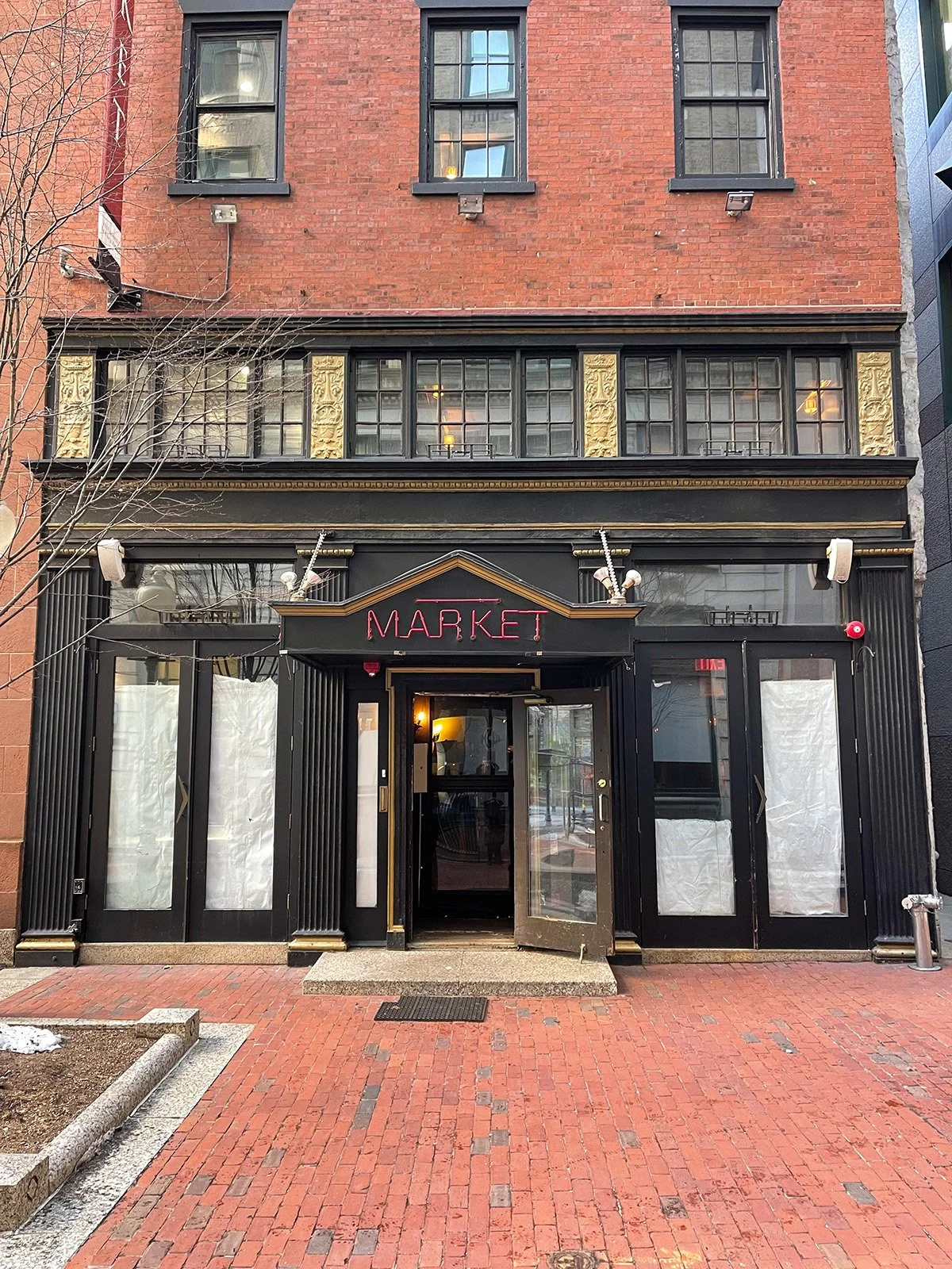 The boarded storefront of a former restaurant in downtown Boston's Financial District, with a vintage Market sign above the entrance.